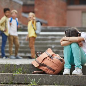A girl sitting on steps with her head down and arms over her knees, while three children stand in the background.