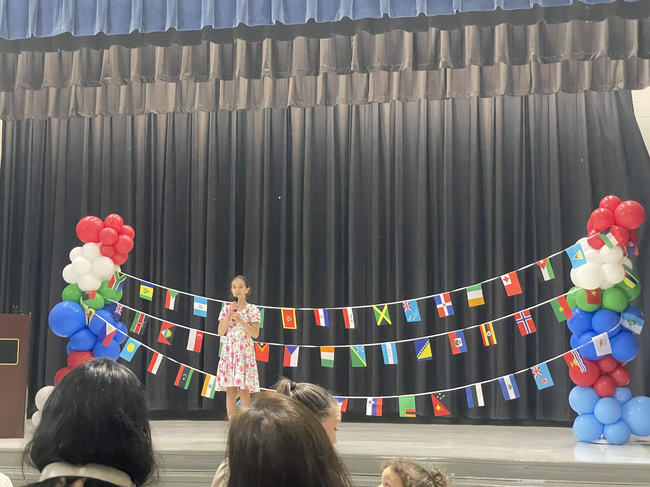Student on stage in front of a banner of flags for a multicultural event.