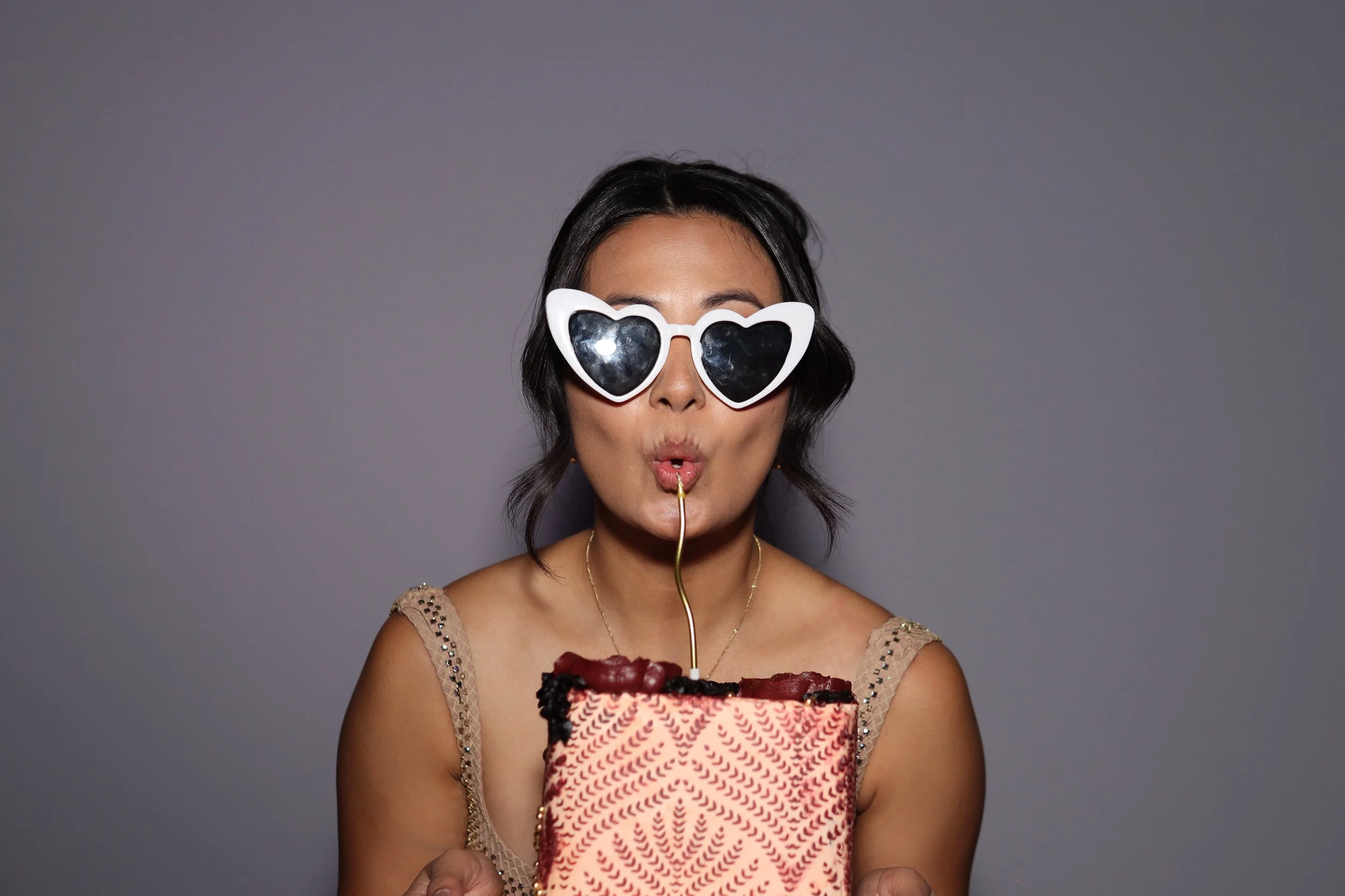 A woman wearing heart-shaped sunglasses is blowing out a candle on a birthday cake.