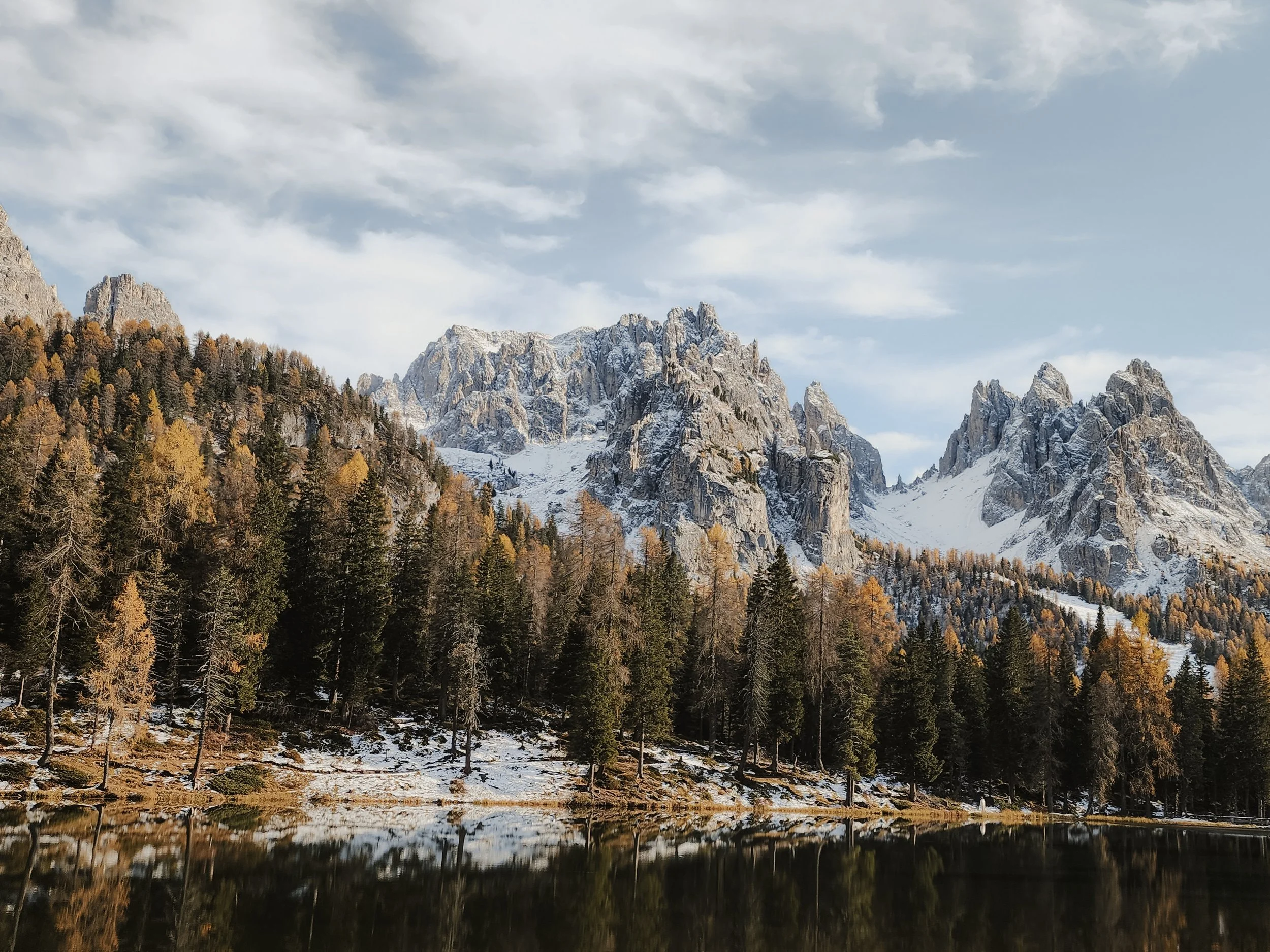 Mountain landscape with snow-capped peaks, evergreen trees, and a calm lake reflecting the scenery.