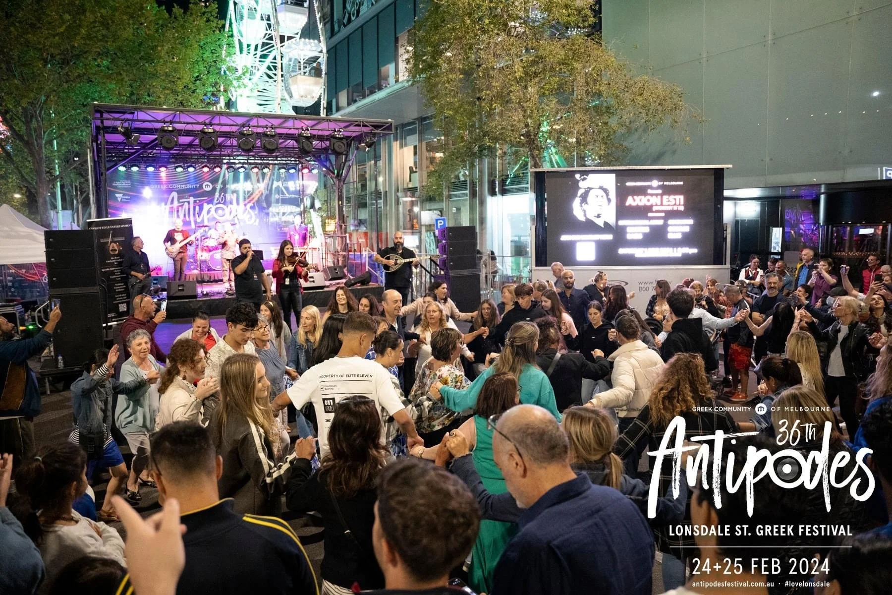A lively crowd of people dancing at the Lonsdale St. Greek Festival, with a stage in the background featuring a live band performing. The scene is vibrant with colorful lights, and information about the 36th Antipodes Greek Festival on February 24 and 25, 2024, is displayed in the lower right corner.