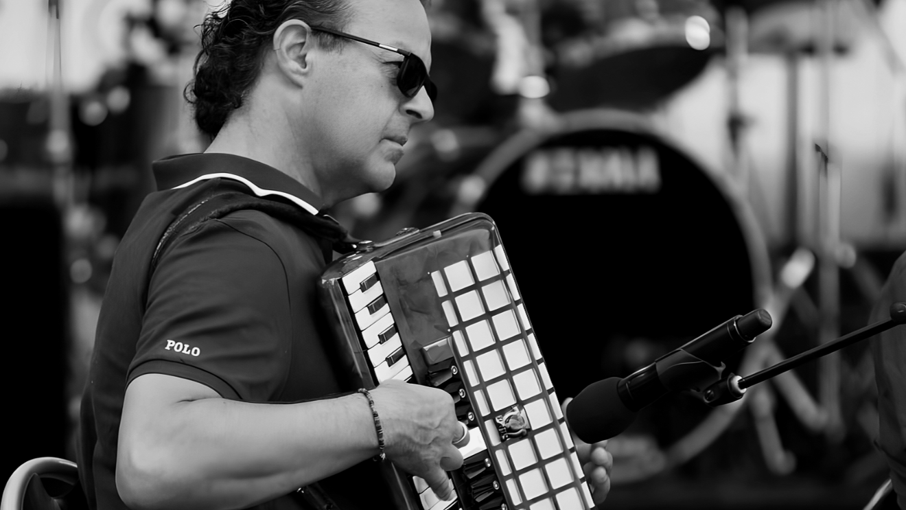 A man wearing sunglasses playing an electronic keyboard attached to a device, with a microphone in front of him.