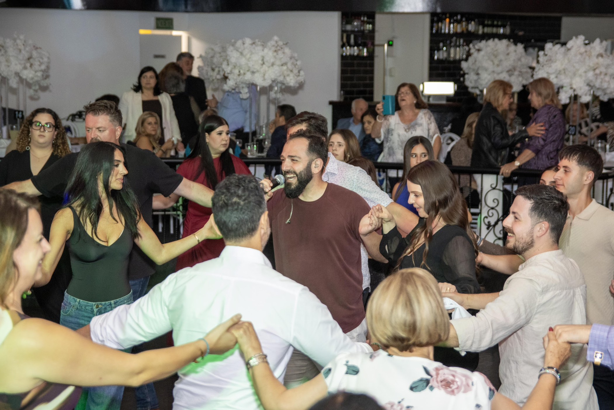 People dancing and singing at a celebration or party, with a man holding a microphone and smiling.