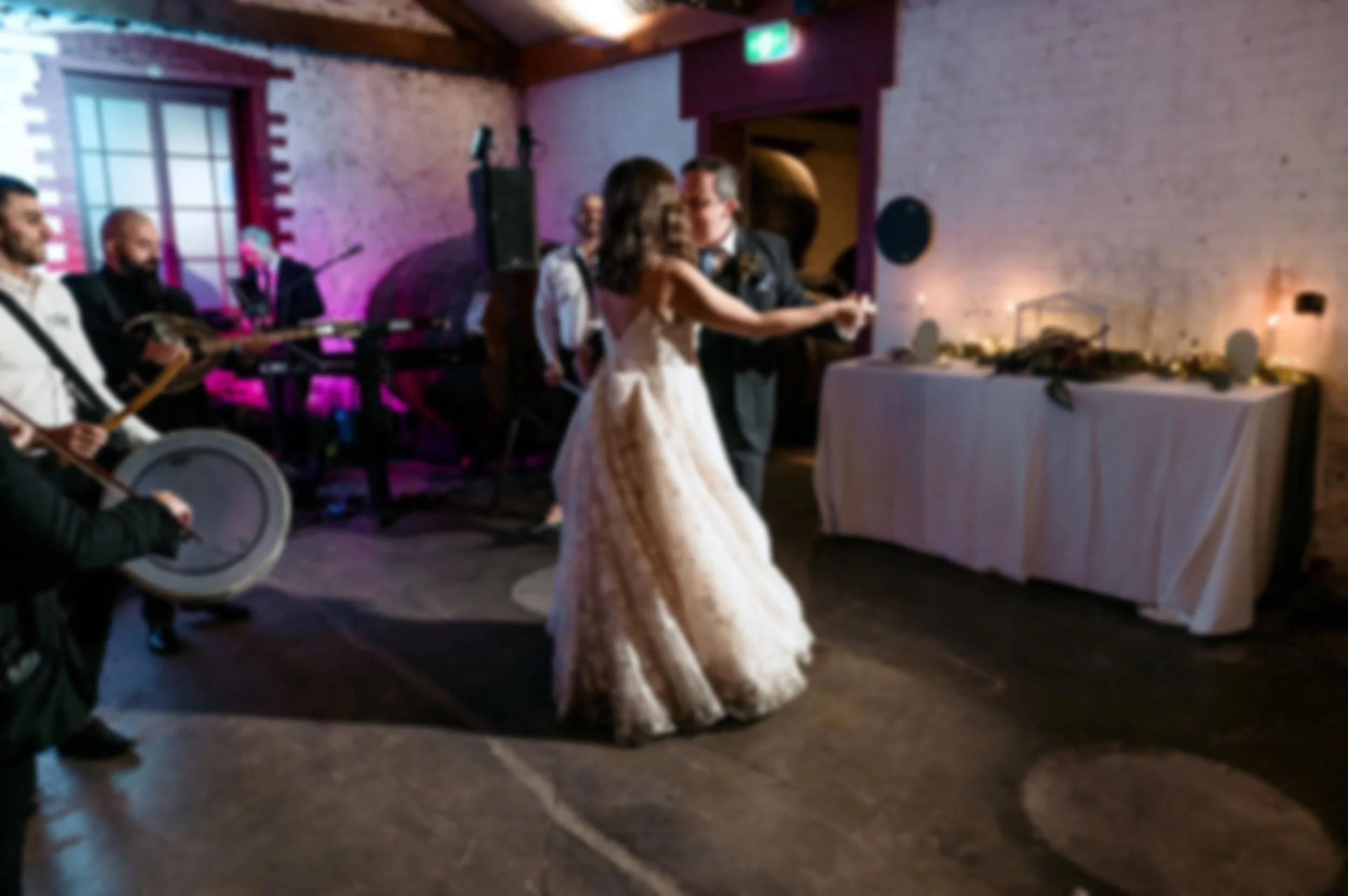 A bride and groom are dancing at their wedding reception, with musicians playing on the left side in a decorated indoor venue.