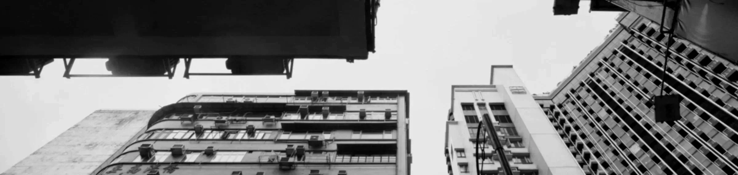 Black and white photograph of tall buildings from a low-angle view, looking up at the sky.
