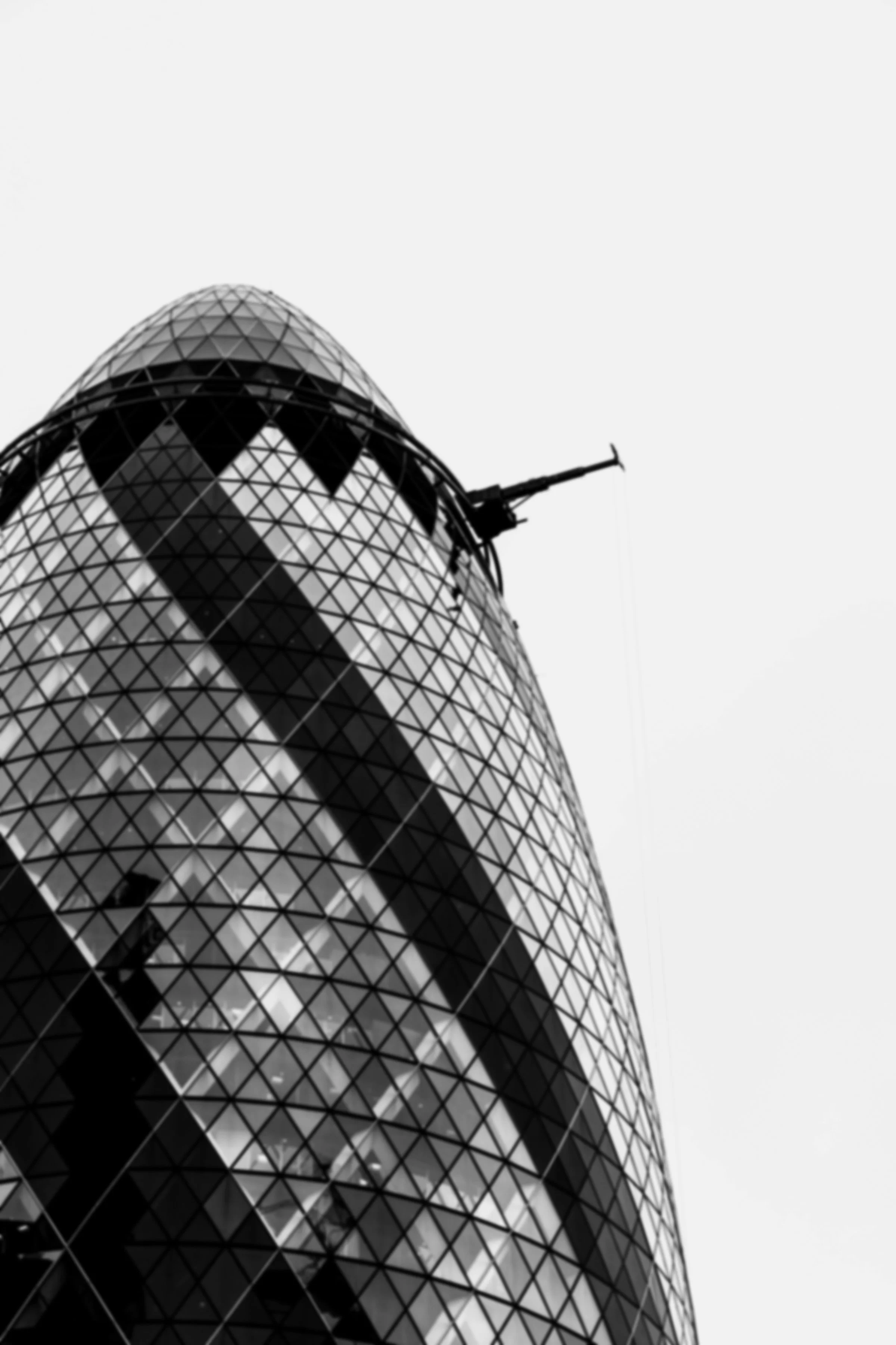 Black and white photo of a modern glass building with a curved, diamond-patterned exterior and a construction crane extending from the top, representing looking up and growth.