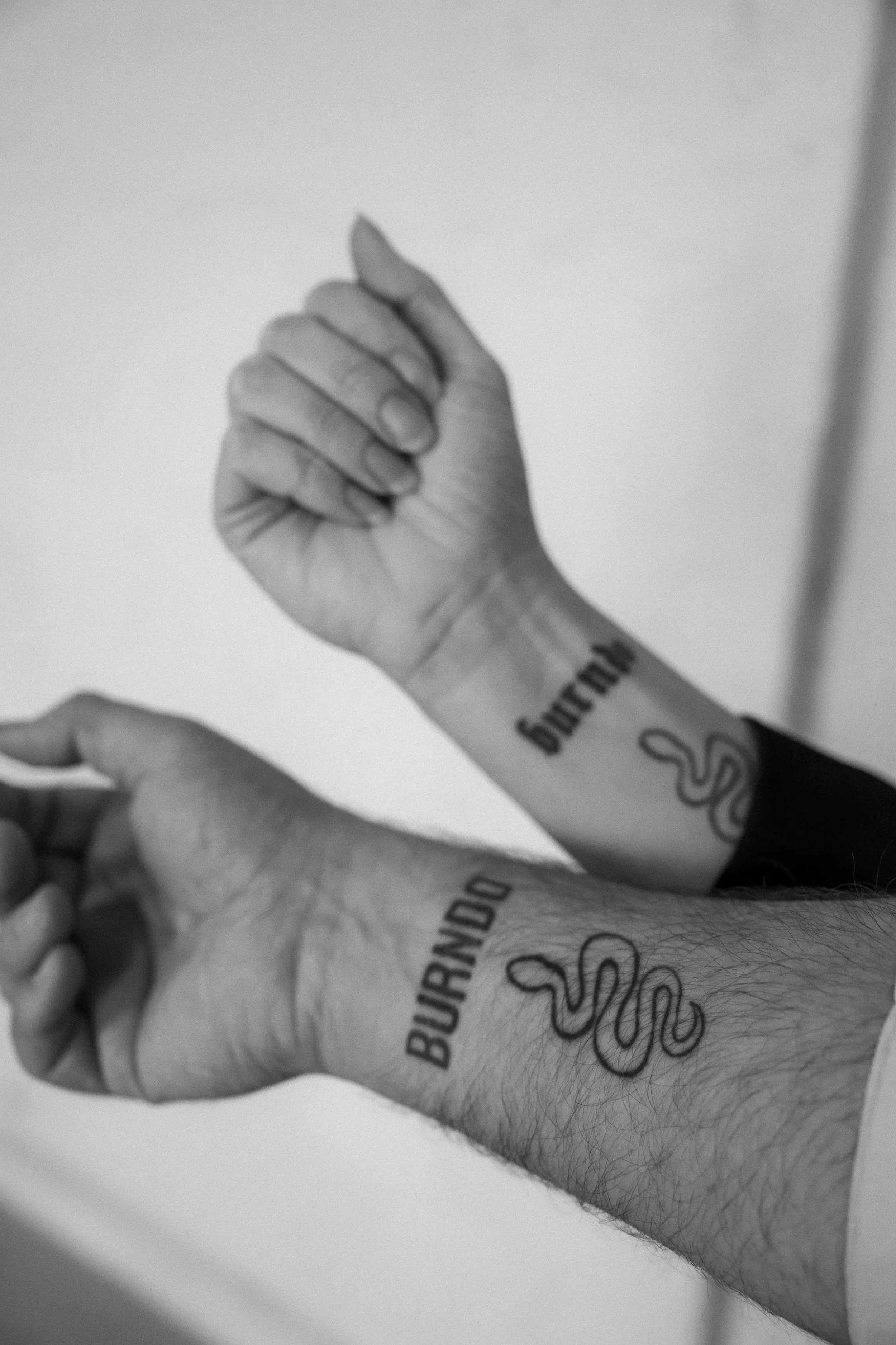 Close-up of two tattooed arms with clenched fists, displaying the words "BURNOUT" and "BURNING" along with a snake tattoo.