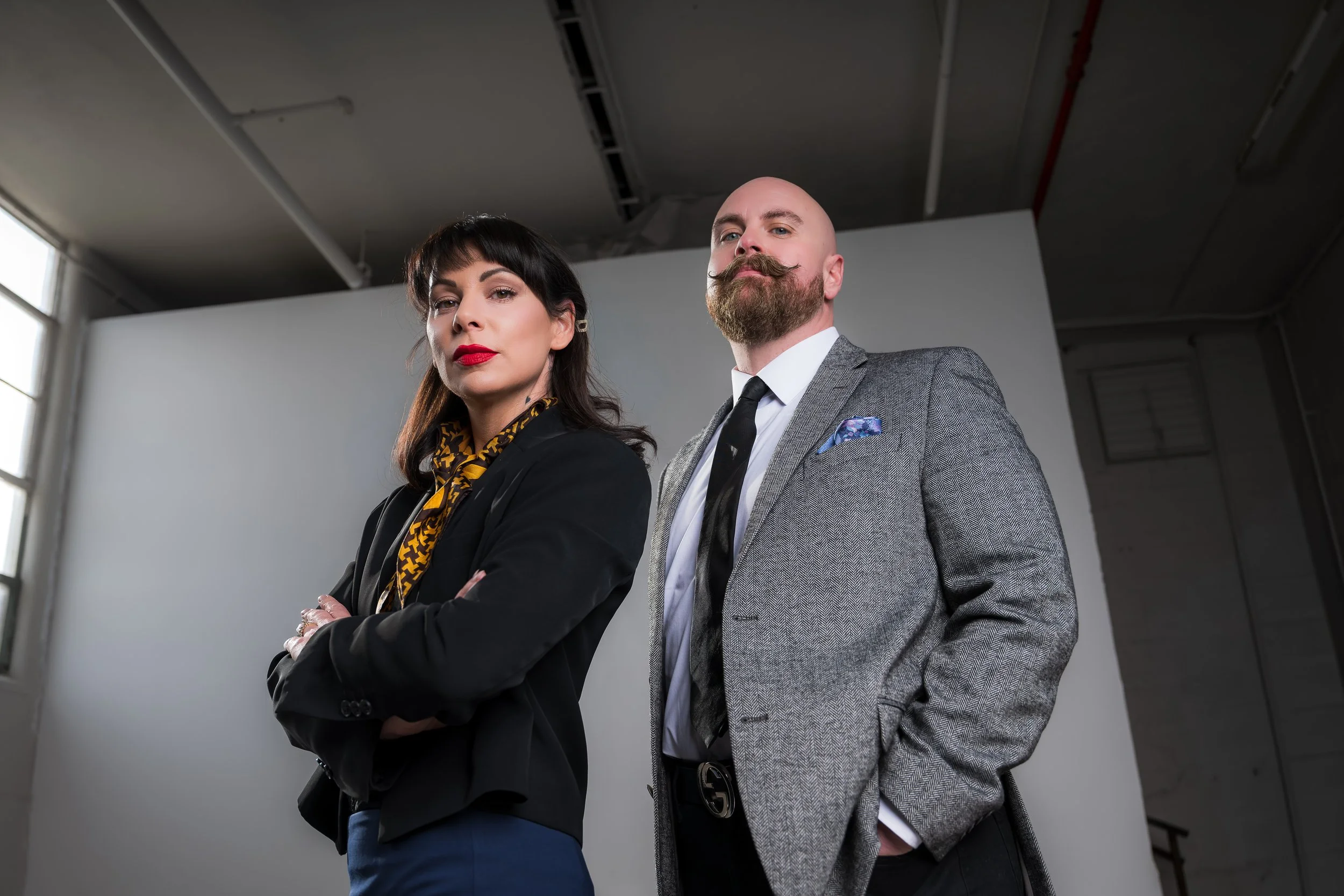A confident woman and man in business attire standing with arms crossed in an office setting.