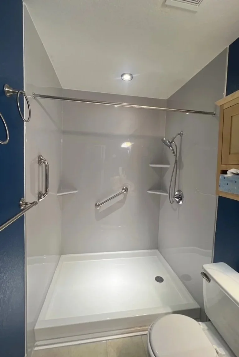 Accessible shower with grab bars, built-in corner shelves, handheld showerhead, and a shower curtain rod.