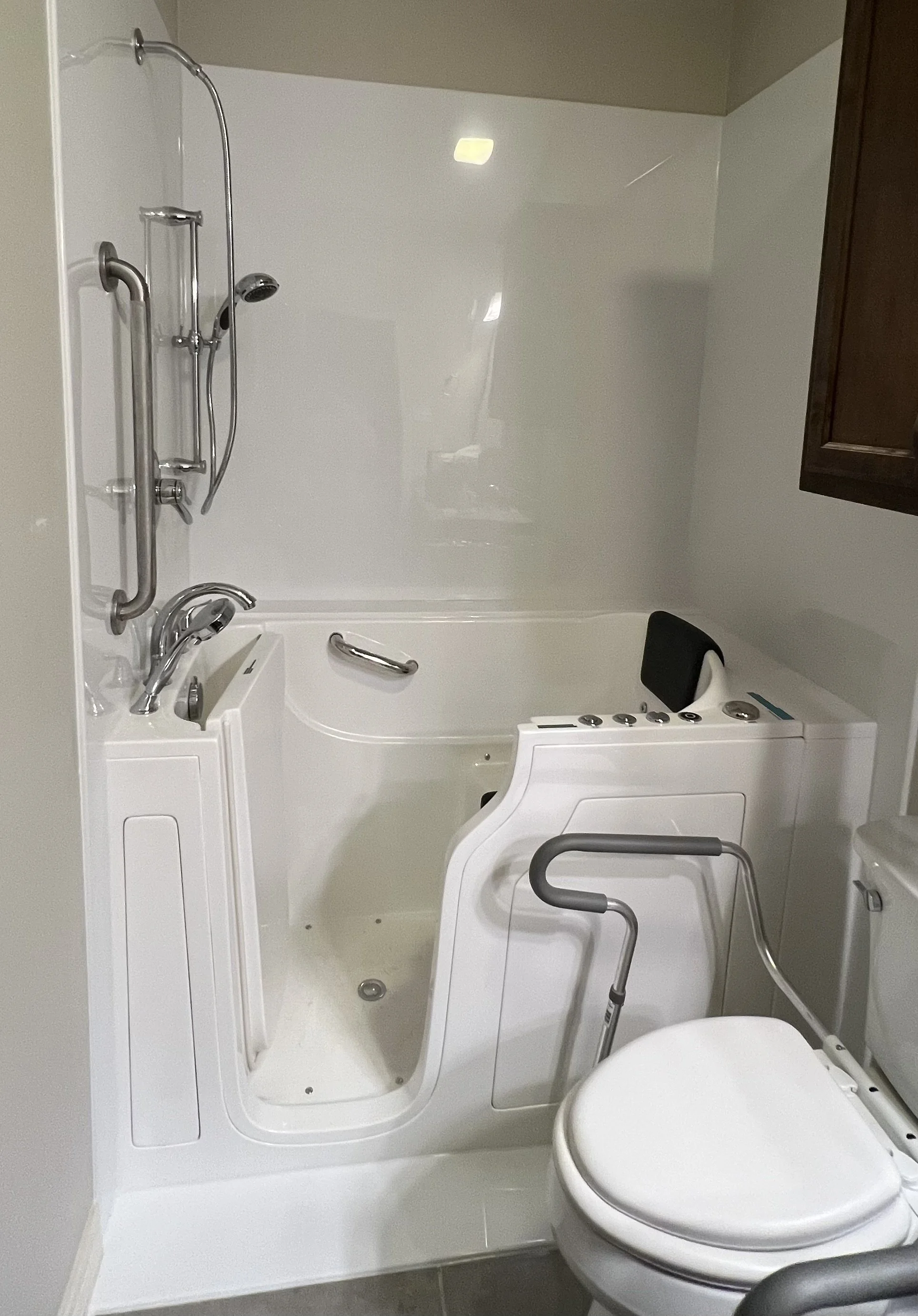A white walk-in tub, a showerhead, grab bars, with a safety rail, and a handheld shower head.