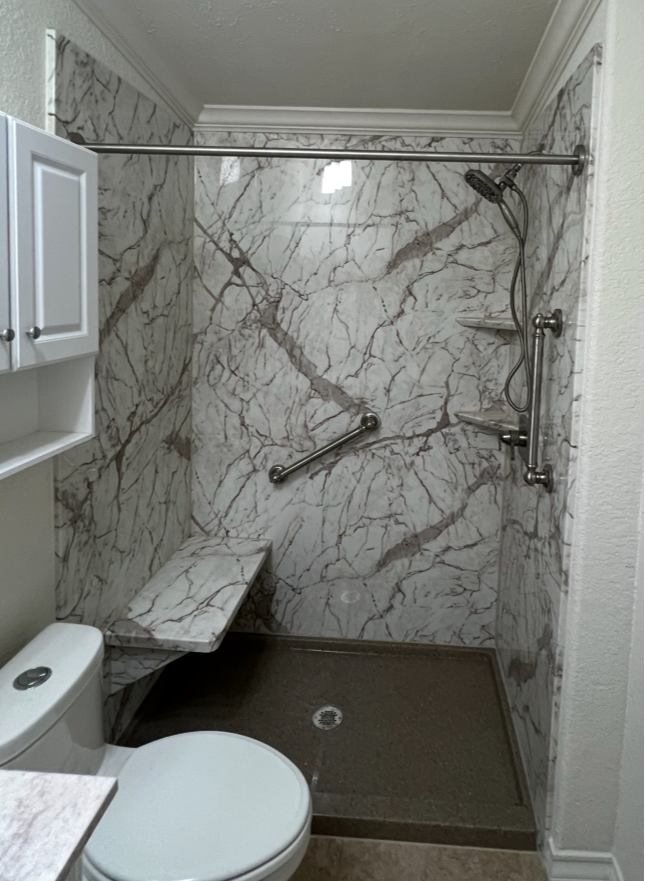 Acrylic shower with marble walls, shelves, and grab bars.