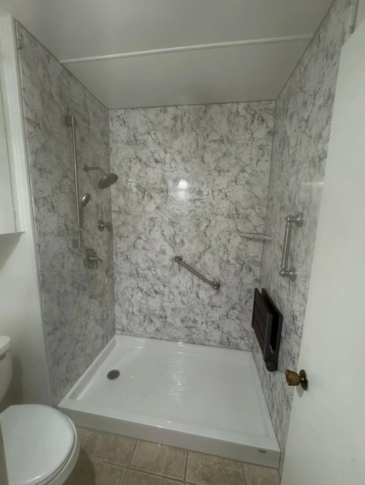 marble shower with grab bars, a shower head, a soap shelf, and a fold down seat.