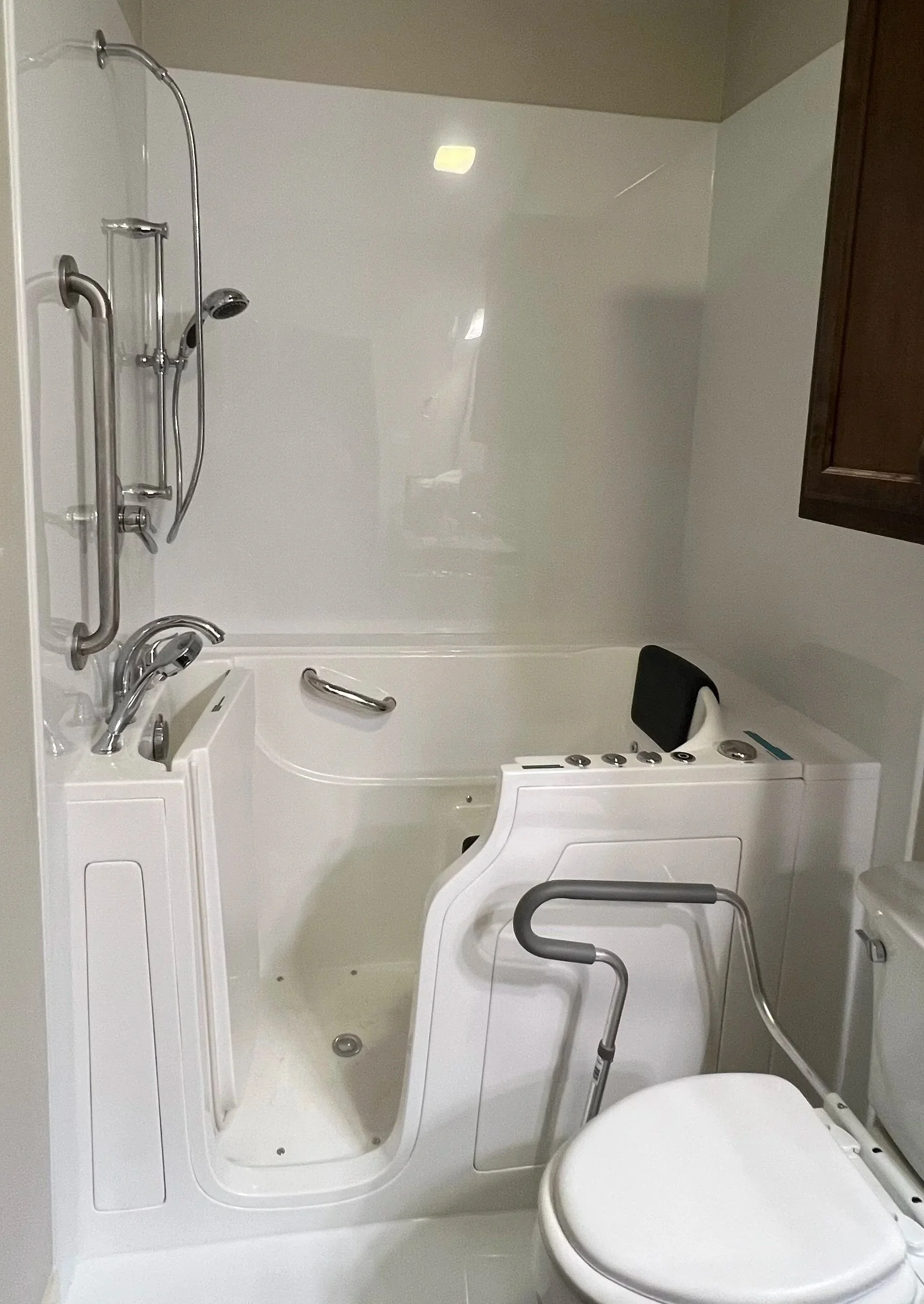 A white walk-in bathtub, handheld shower head, grab bars, and a slide bar.