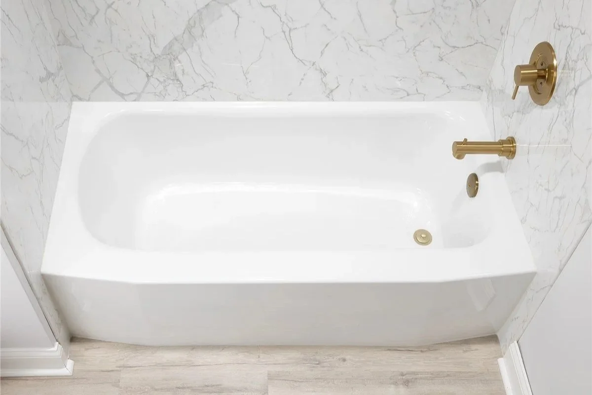  white bathtub with gold fixtures, surrounded by marble-patterned acrylic walls.