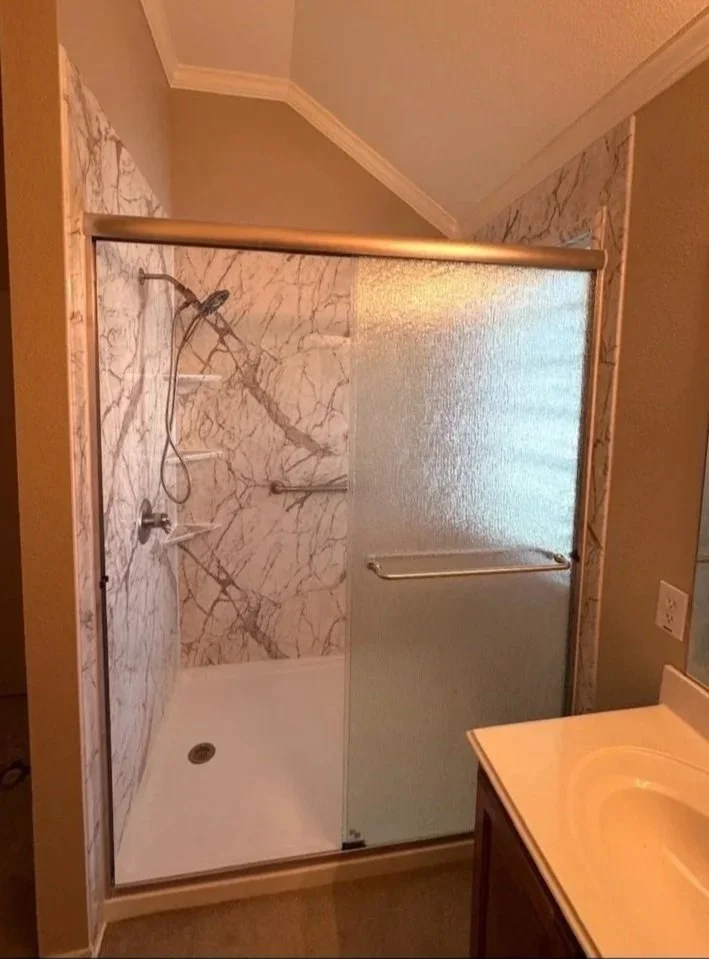 Bathroom acrylic shower, a glass door with a frosted pattern, a hand-held shower wand, and metal grab bars.