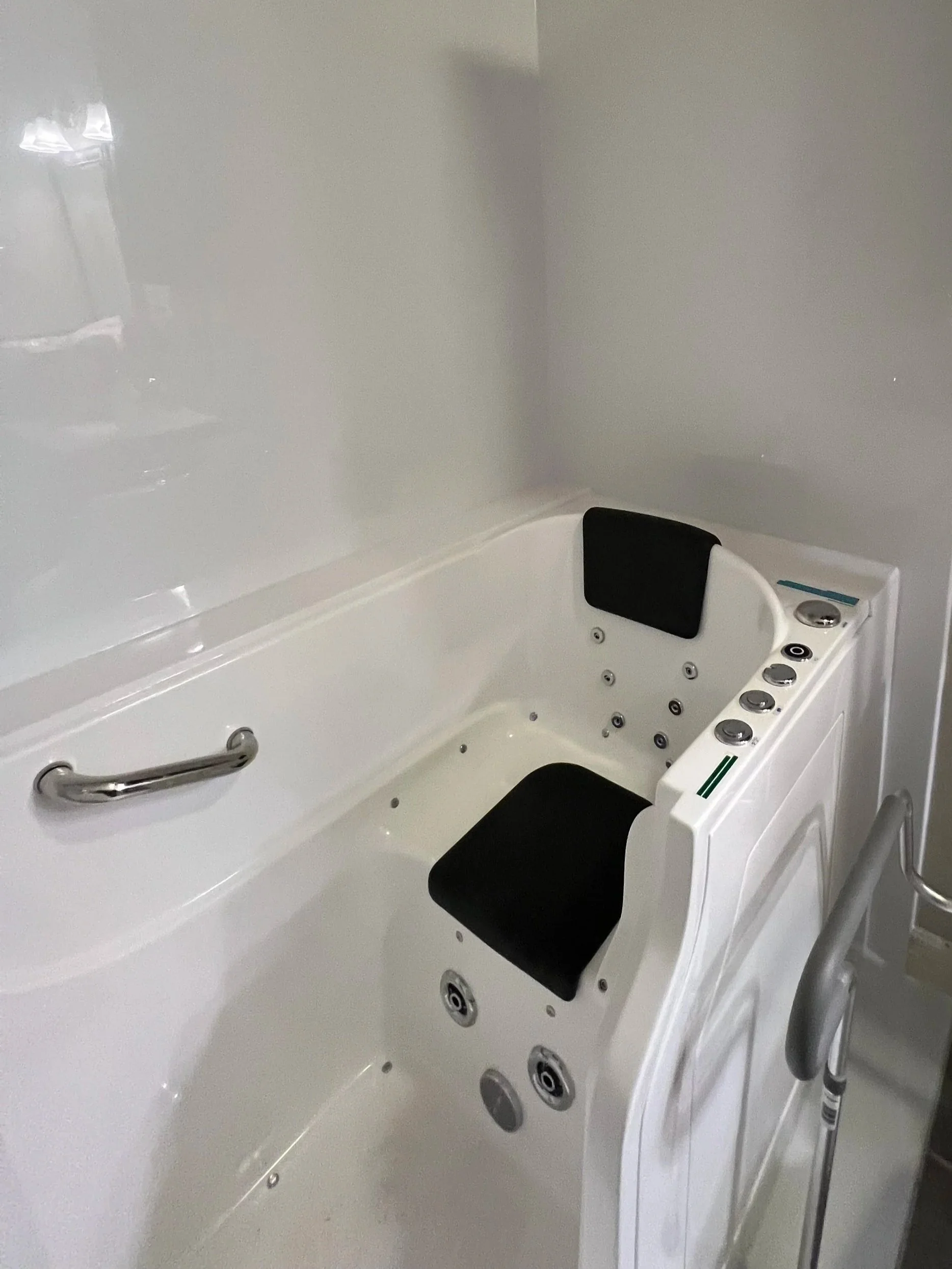 A white walk-in bathtub with cushioned headrests, built-in control panel, and massage jets, designed for therapeutic bathing with accessibility features.