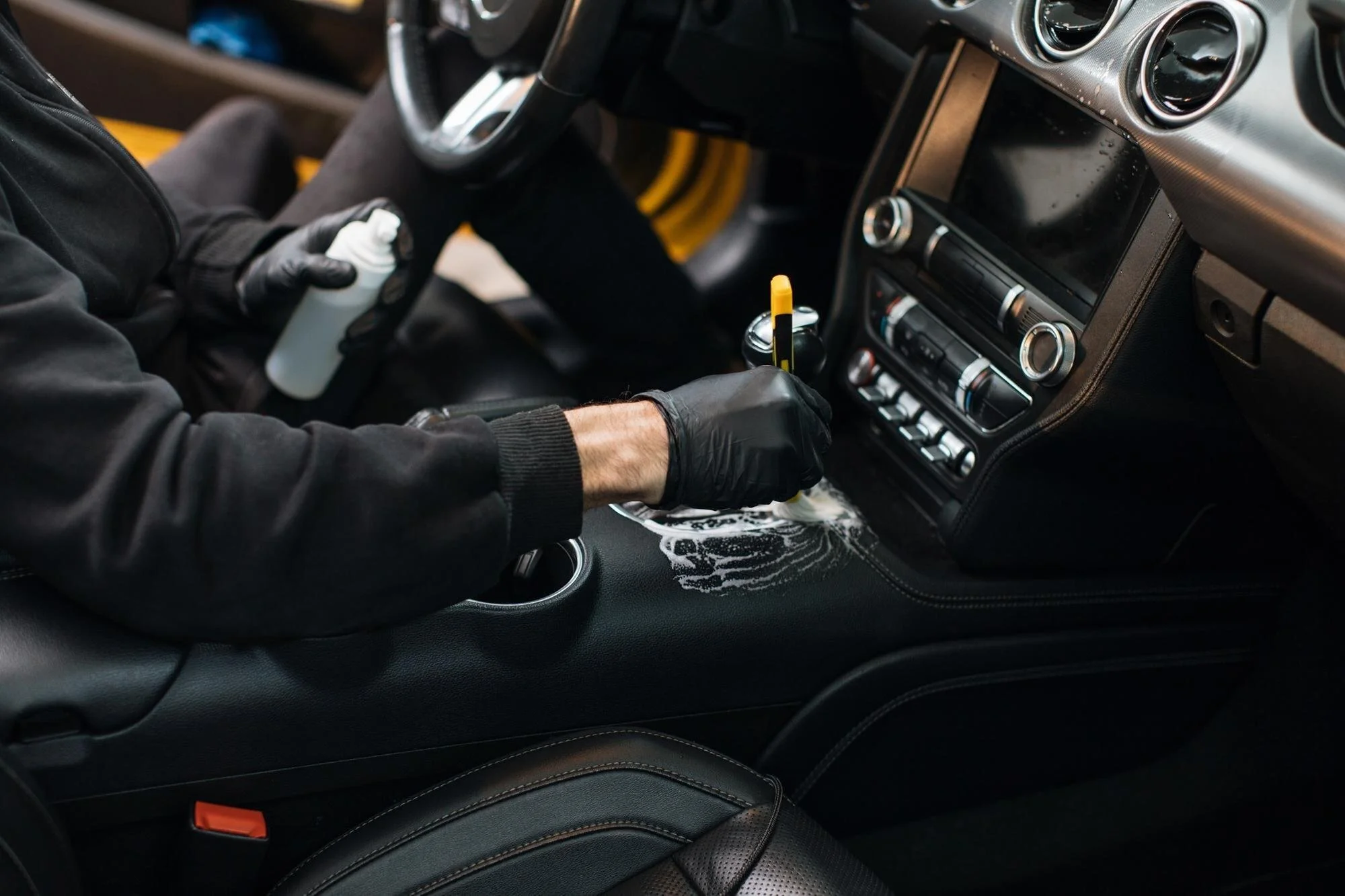 Person cleaning car interior with foam, holding spray bottle and brush