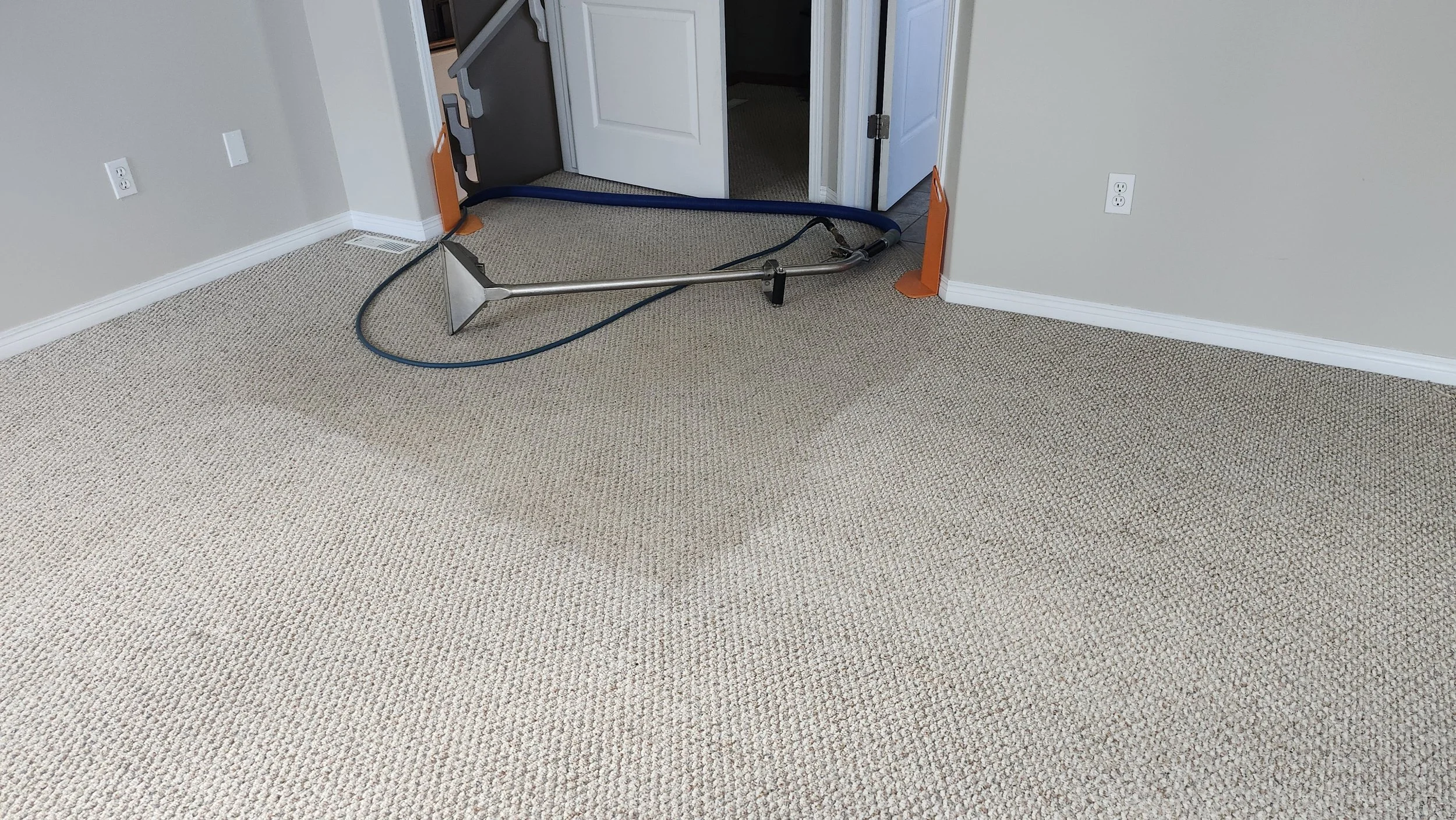 A room being cleaned by hot water extraction, or steam cleaning. The carpet wand and corner and wall protection near the door