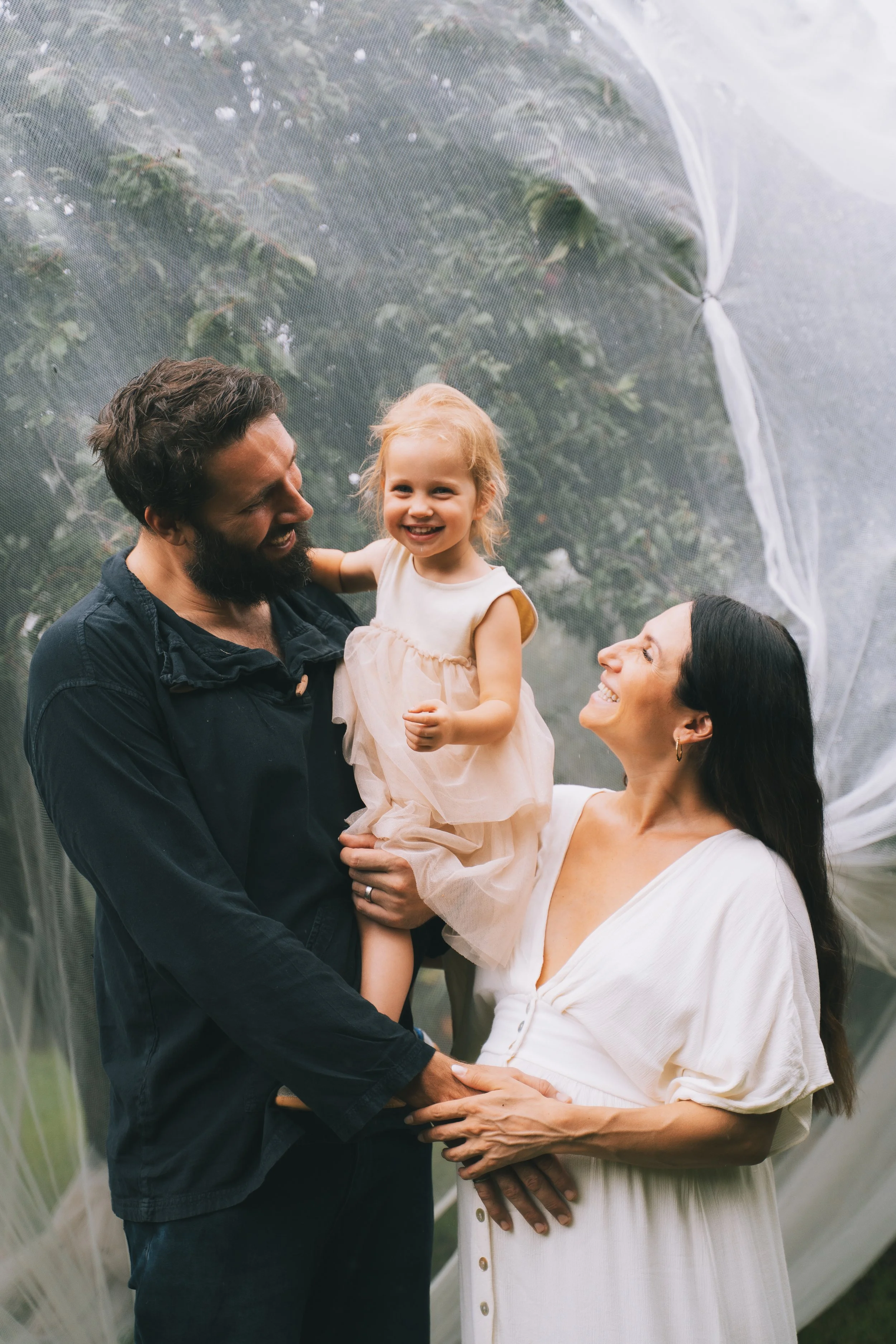 Family of three, a man, a woman, and a young girl, sharing a joyful moment outdoors during daytime.