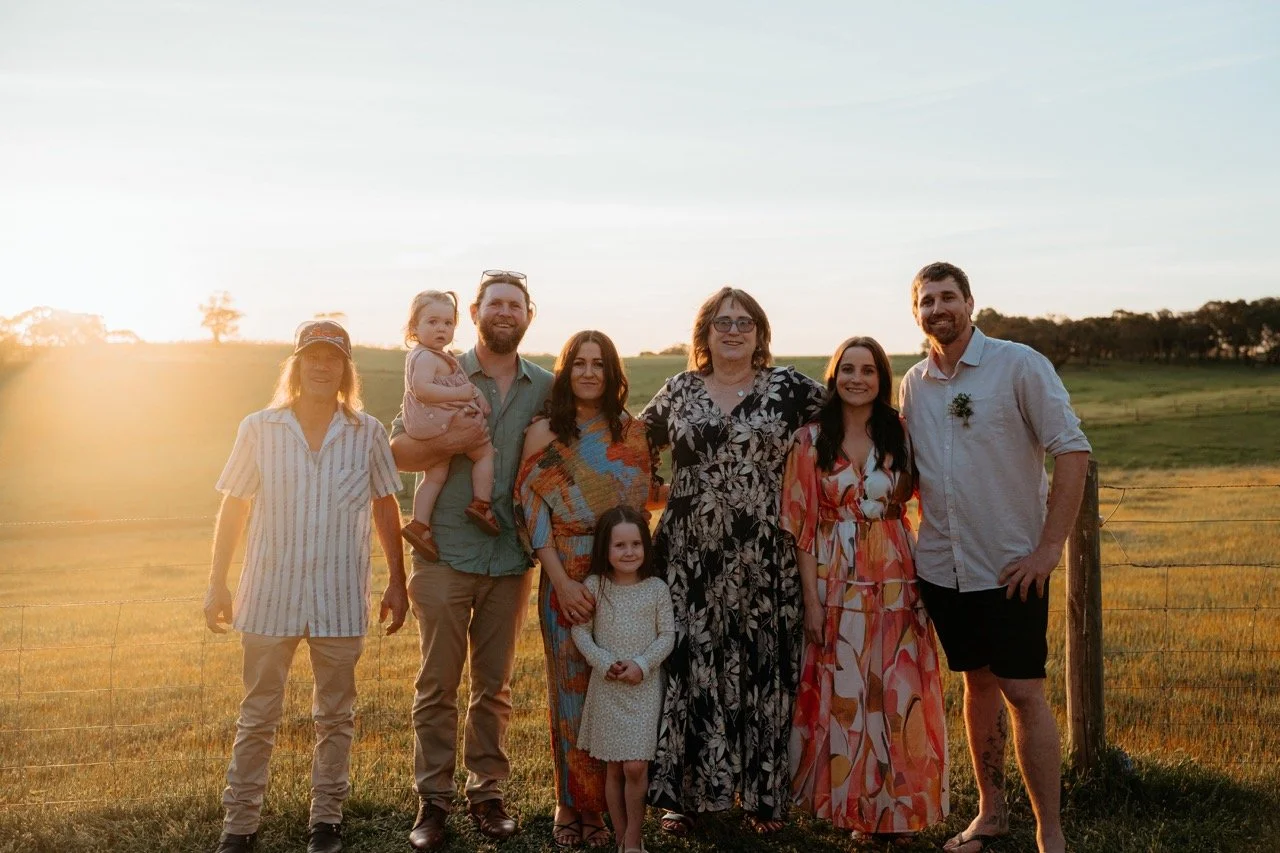Family group standing outdoors in a field during sunset, smiling at the camera.