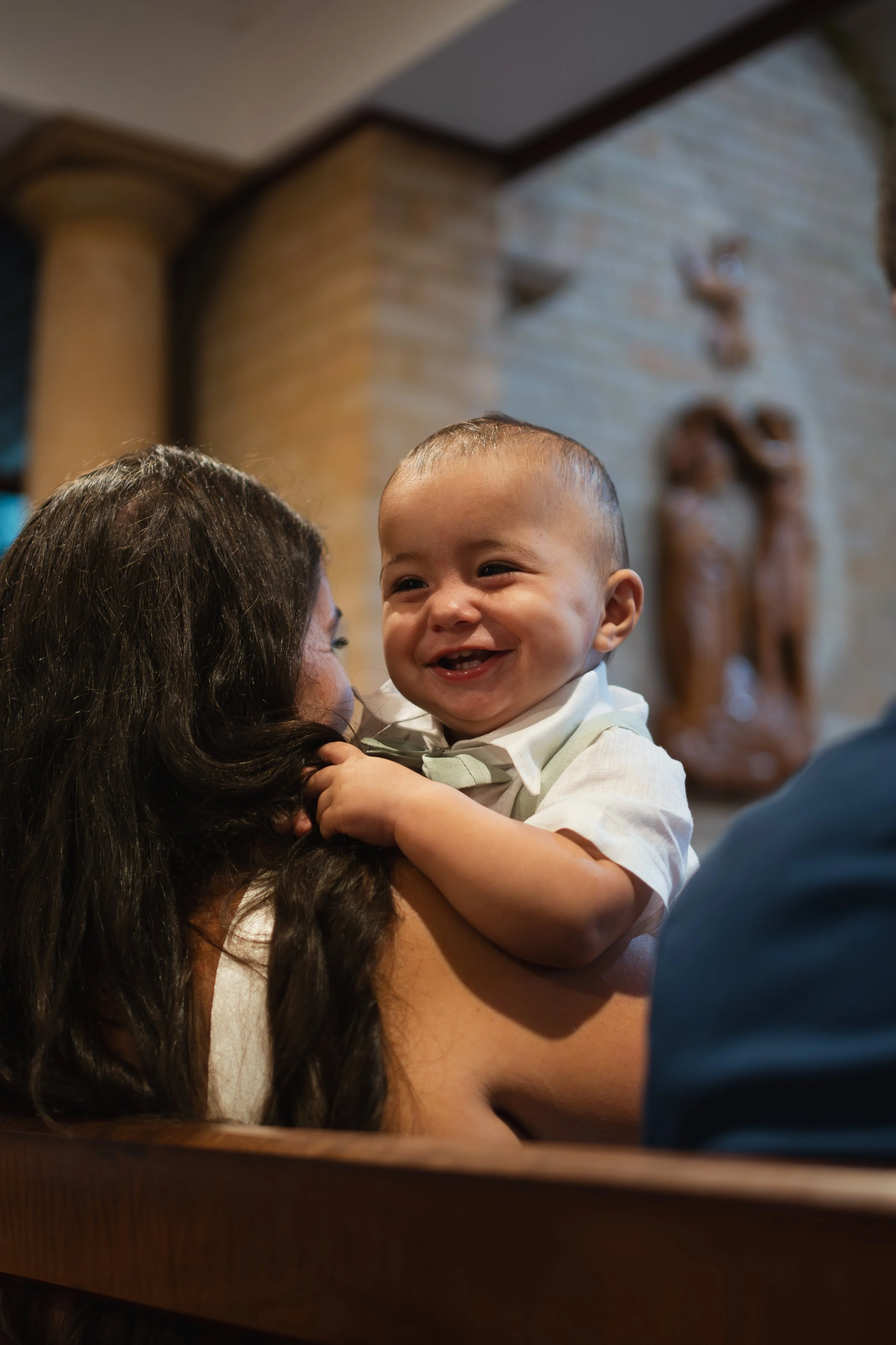 A happy baby with a big smile being held by a woman with long dark hair.