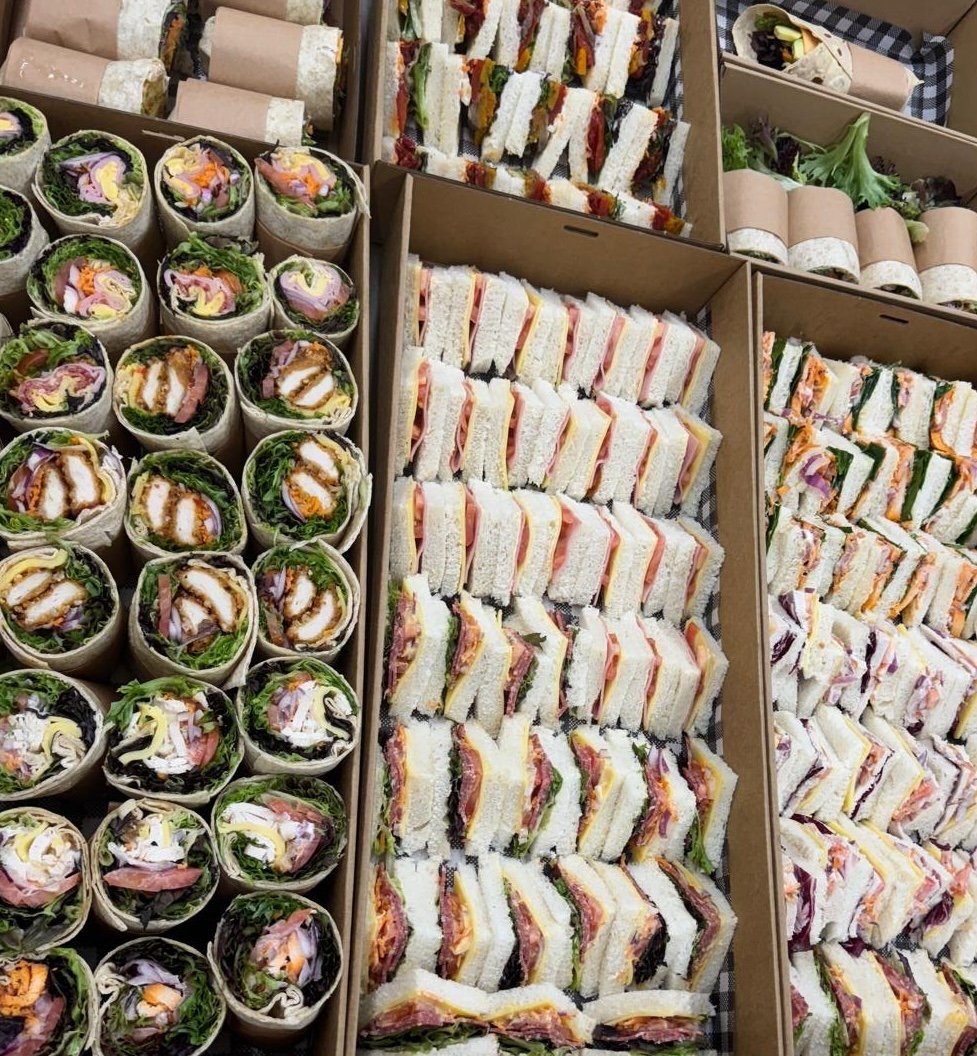 Various types of sandwiches and wraps arranged in boxes, including club sandwiches, veggie wraps, and assorted rolled wraps.