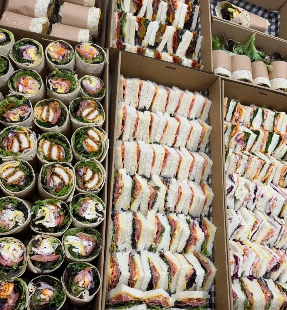 A variety of pre-made sandwiches and wraps arranged in boxes, including wraps filled with greens and meats on the left and multiple types of sandwiches with various fillings on the right.
