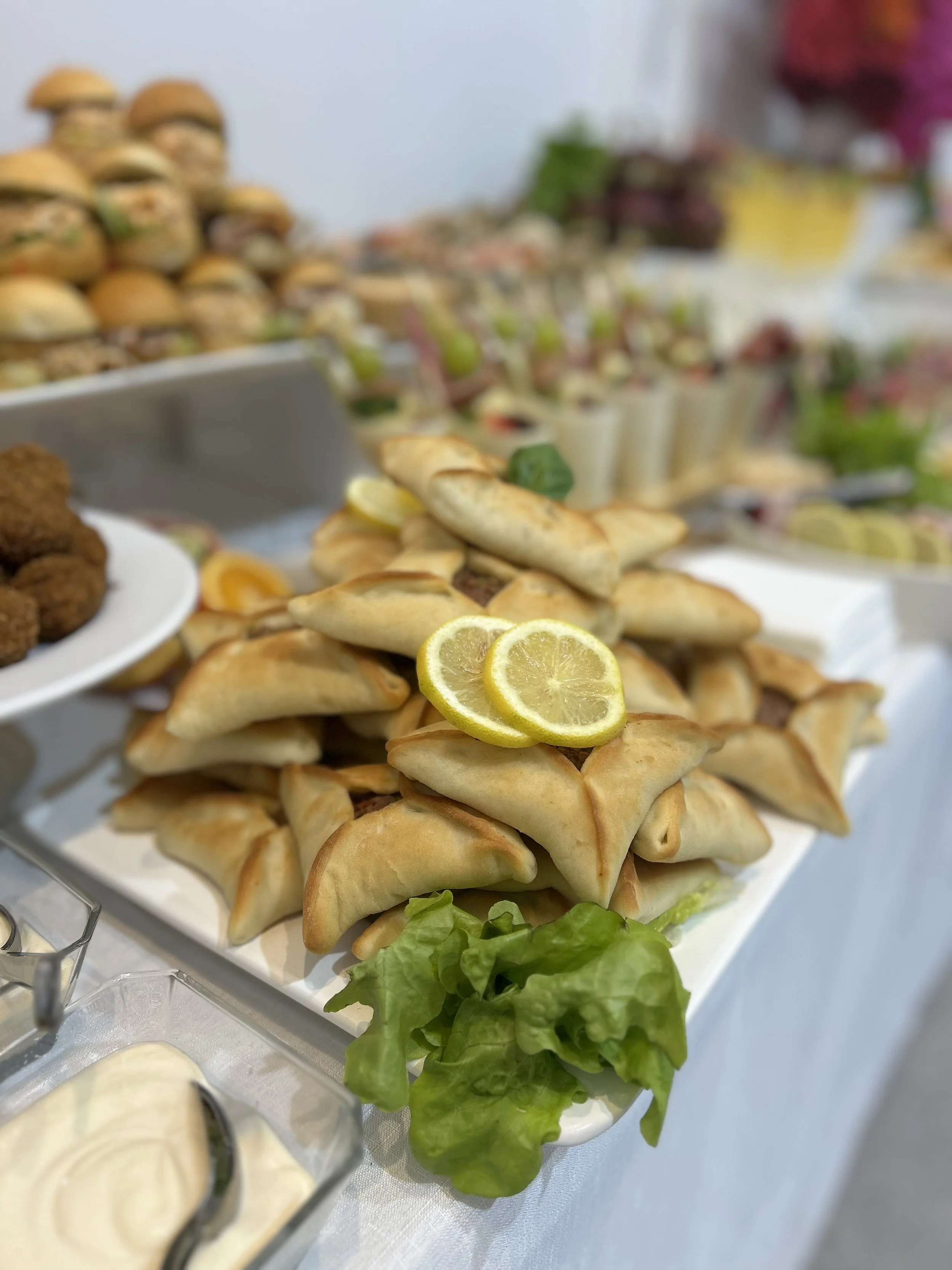 Tray of samosas garnished with lemon slices and lettuce, part of a buffet with other dishes and appetizers in the background.