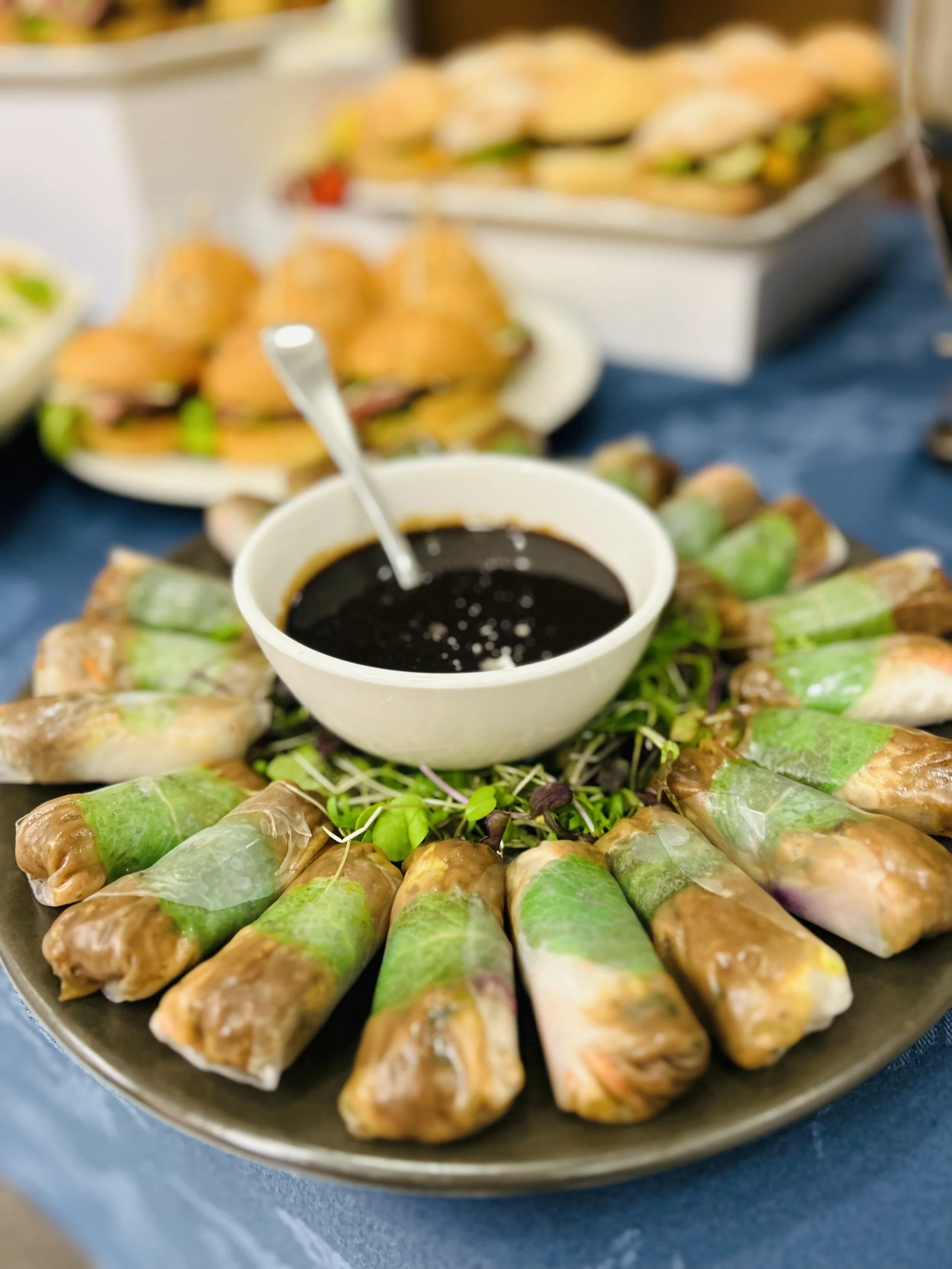 Spring rolls with dipping sauce on a plate, with sandwiches in the background.