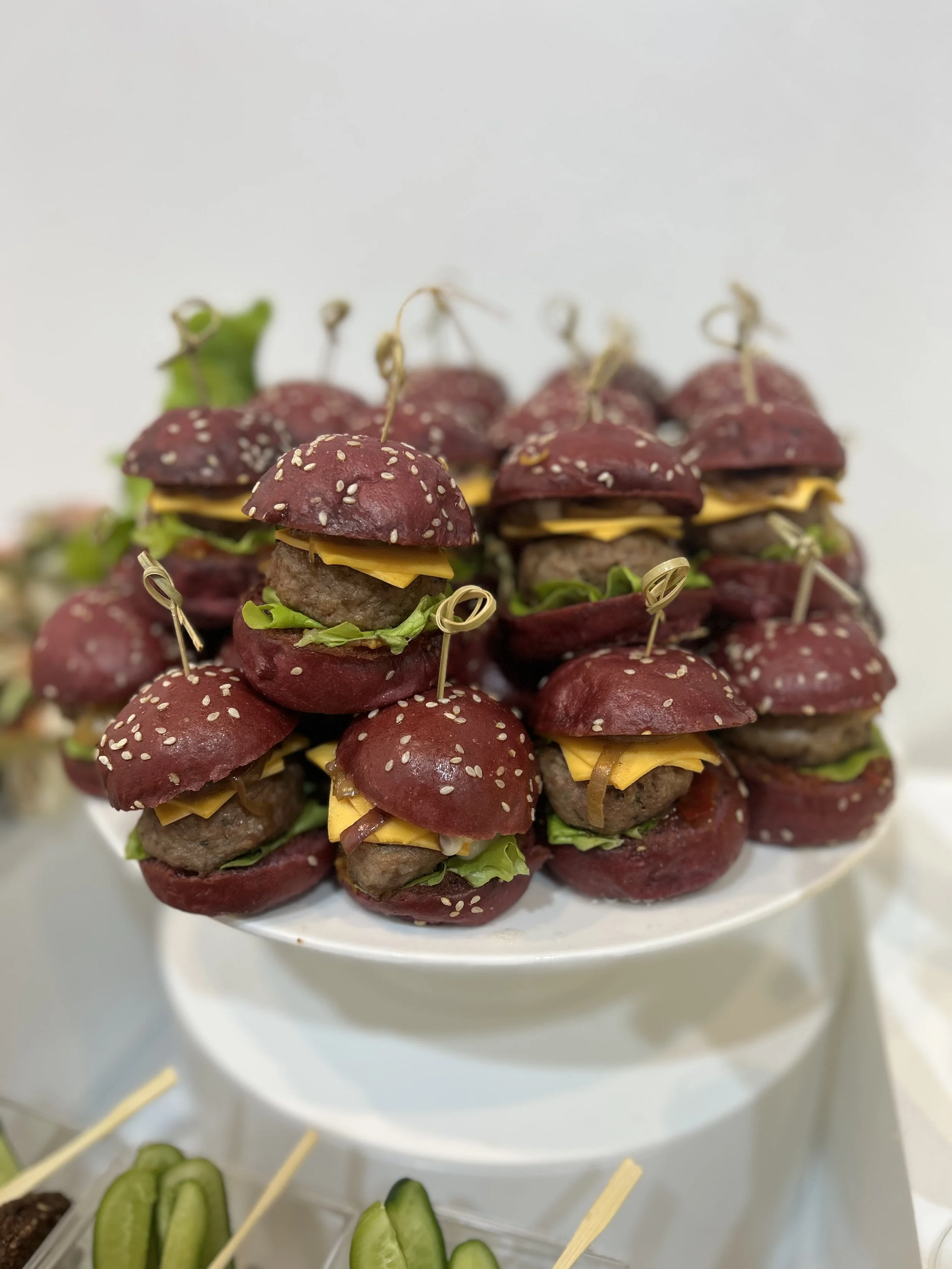 Mini sliders with purple buns, cheese, lettuce, and small burger patties, served on a white platter.