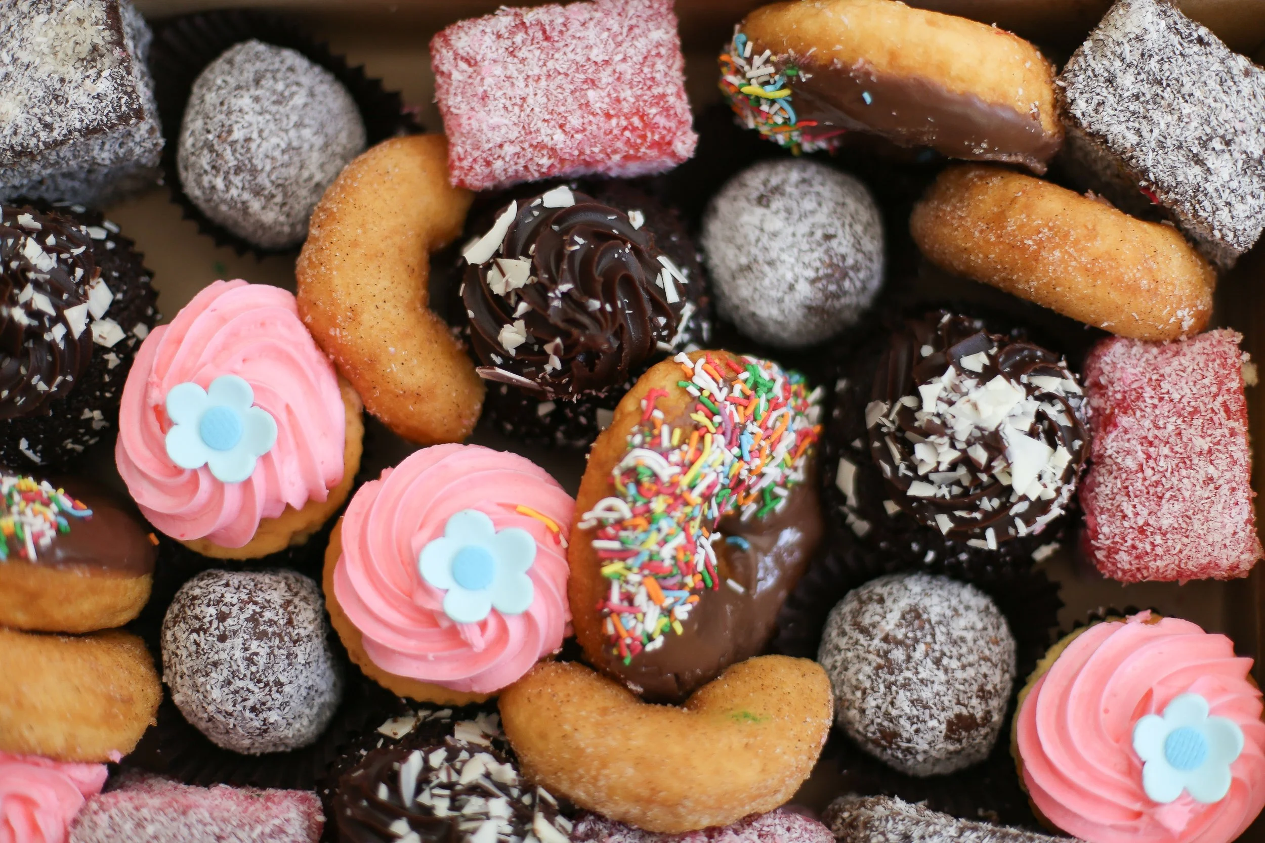 Variety of decorated cookies, including cupcakes with pink icing and blue flowers, chocolate-dipped cookies with sprinkles, and sugar-coated treats.