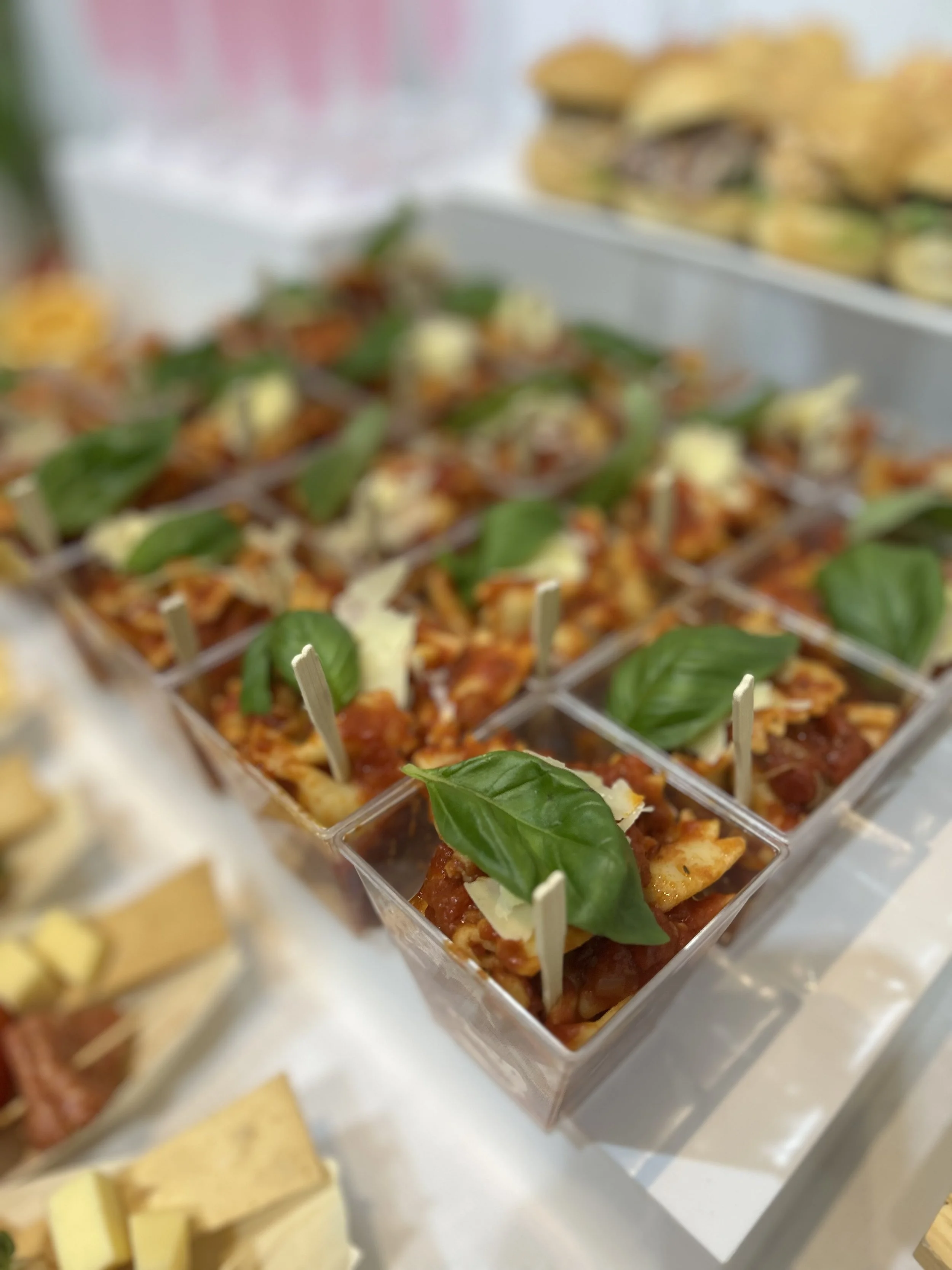 Miniature savory cups filled with spaghetti, topped with cheese and garnished with fresh basil leaves.