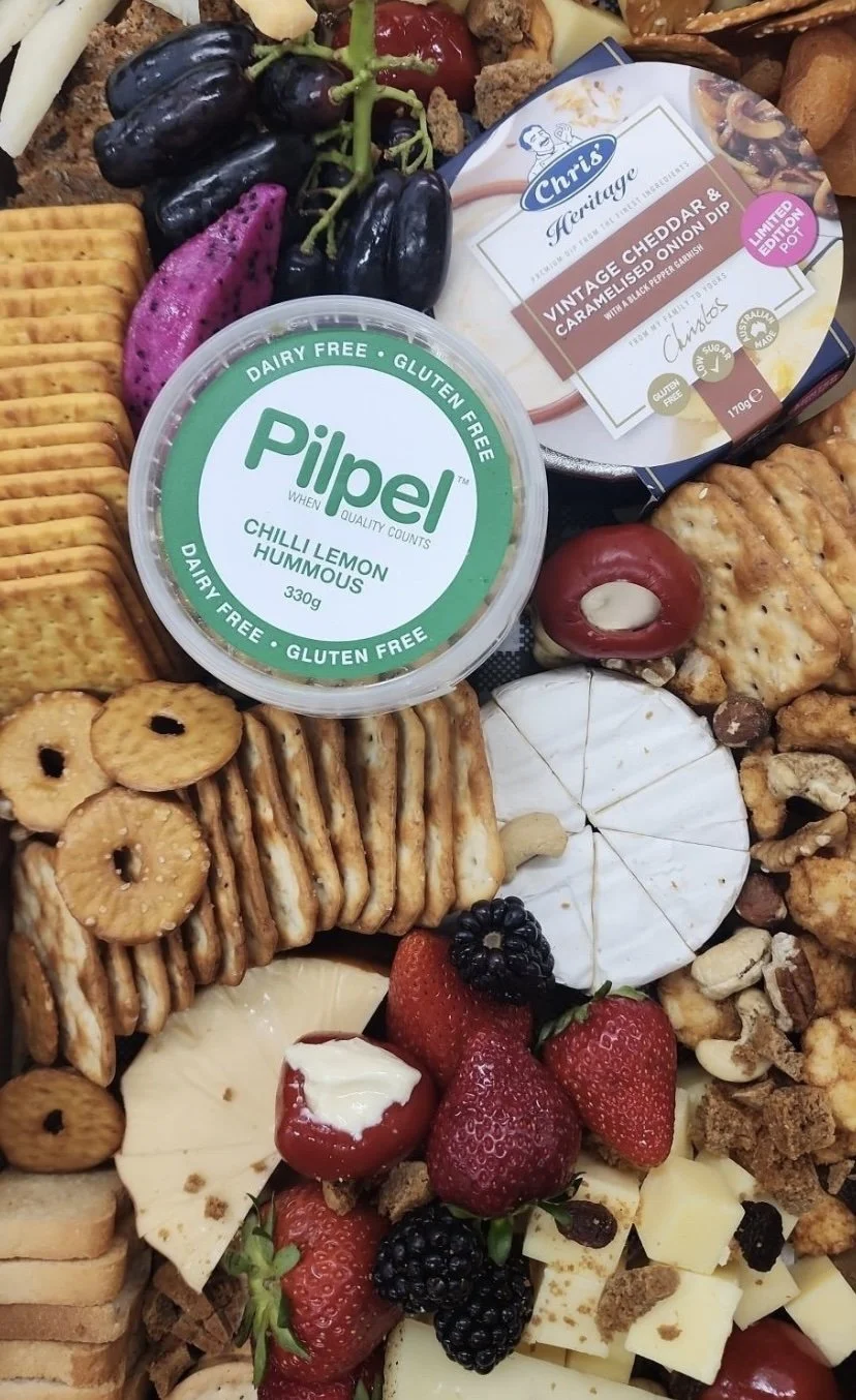 A variety of snacks and foods, including grapes, strawberries, blackberries, cheese, crackers, hummus, and a cheese dip.