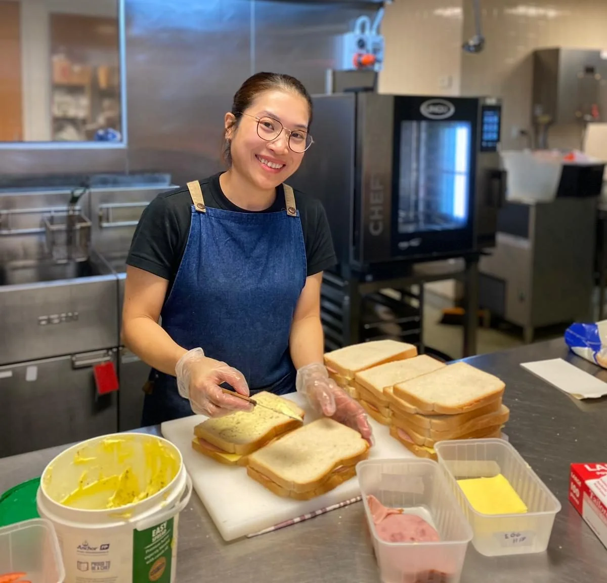 Woman preparing sandwiches with sliced bread, cheese, and ham in a kitchen.