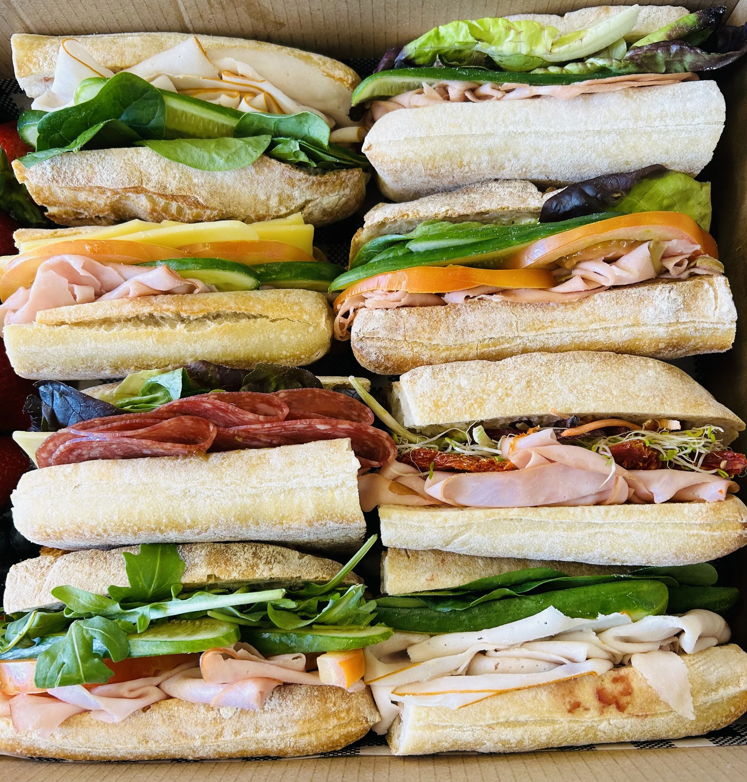 Assorted subs with various meats, cheeses, lettuce, and vegetables in baguette-style bread.