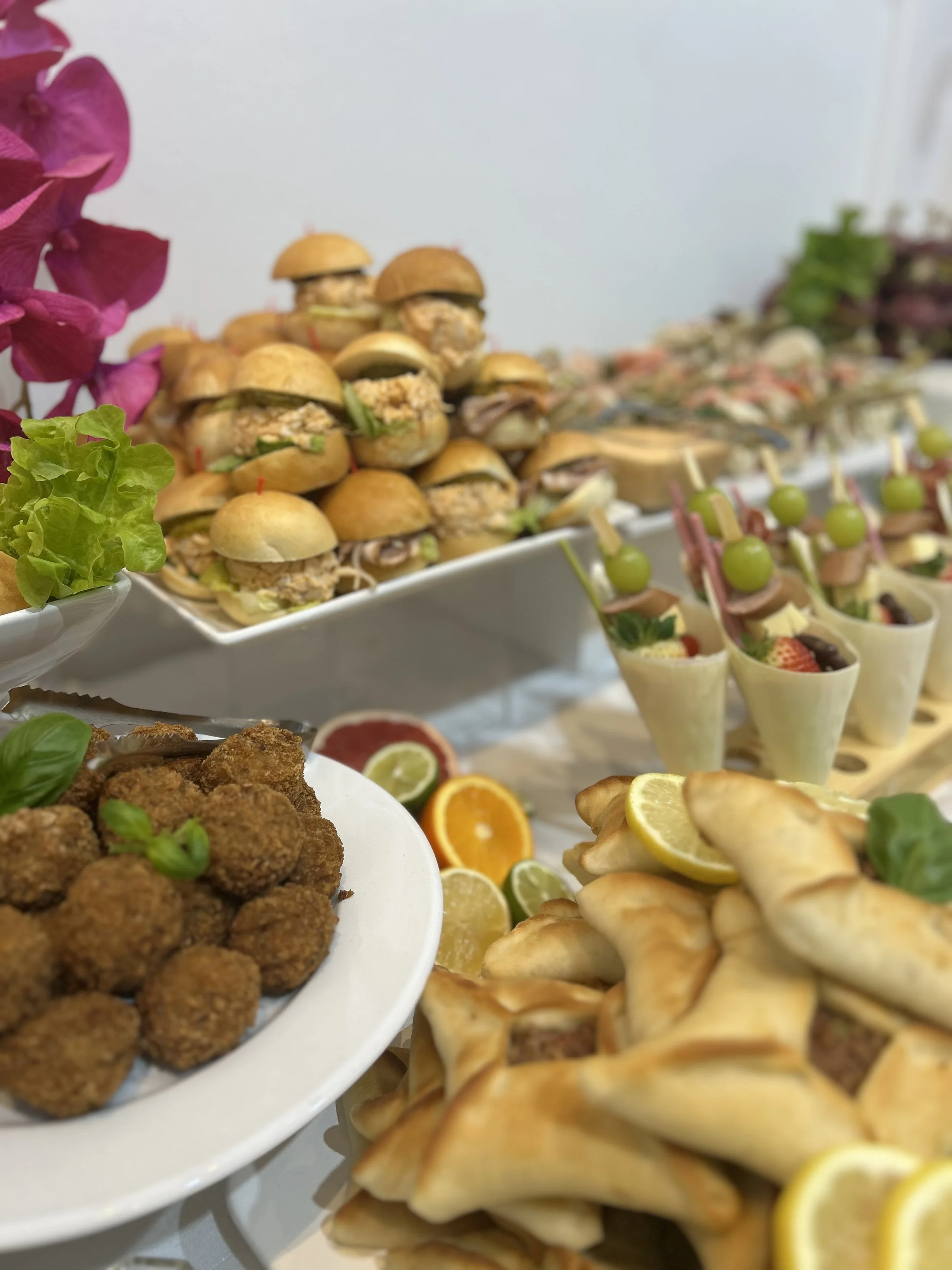 A variety of appetizers including mini sandwiches, fruit cups, fried bites, and puff pastry pockets arranged on a table.