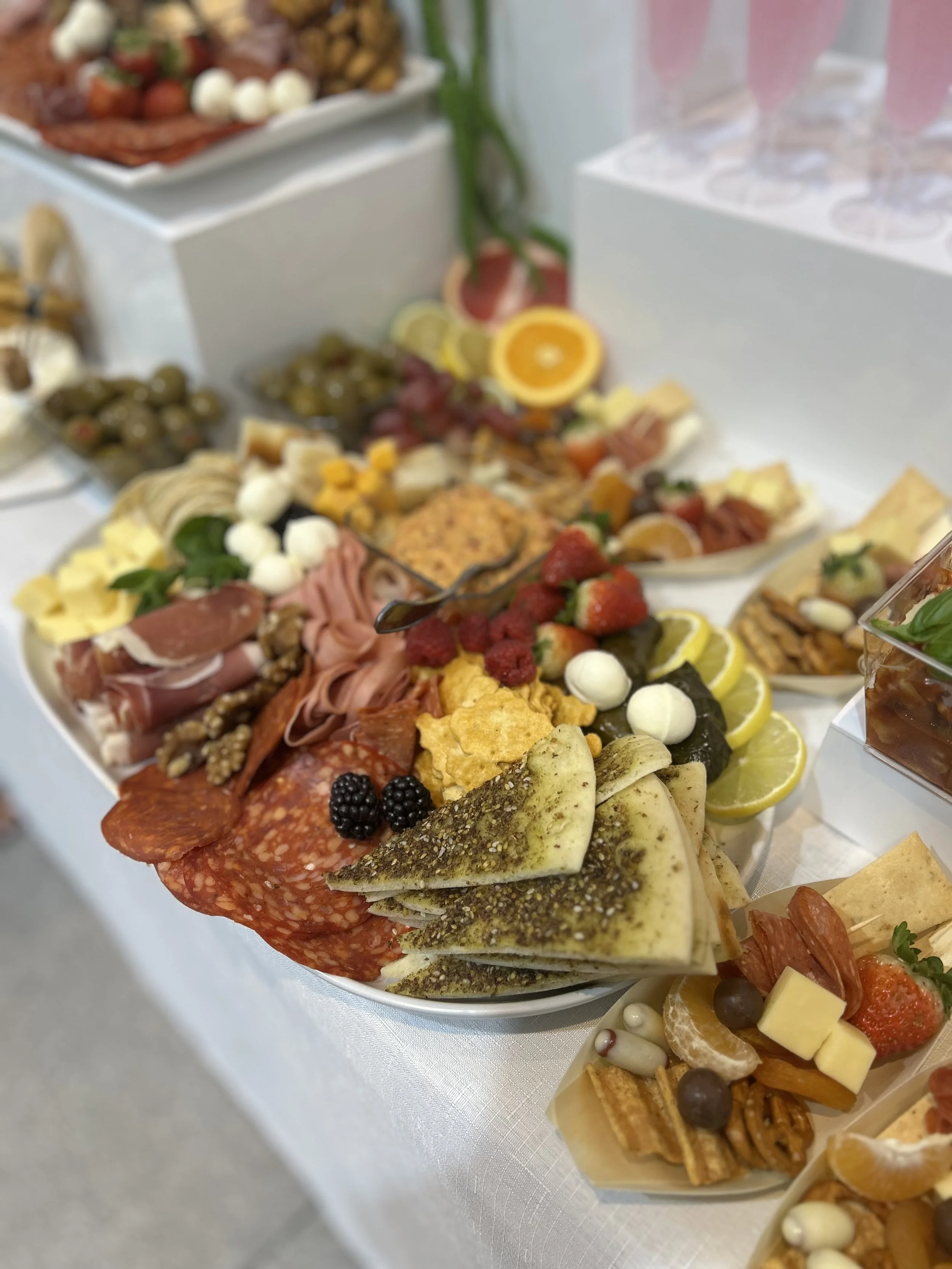 Assorted appetizers and snacks including cheeses, meats, crackers, strawberries, blueberries, blackberries, and lemon slices on a buffet table.