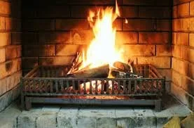 A lit fireplace with burning logs and bright flames, surrounded by brick and metal.