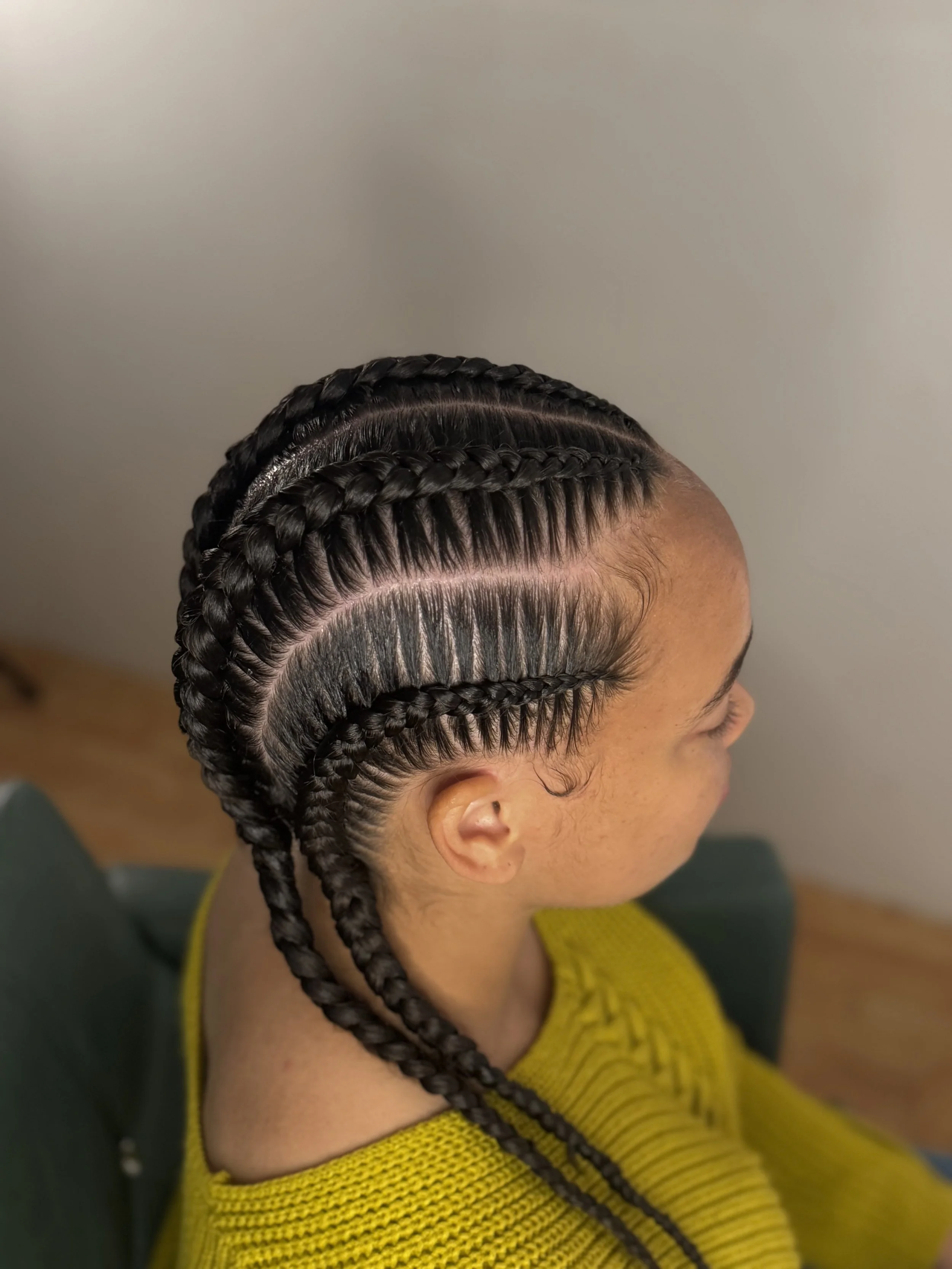 A woman with neatly braided cornrows, styled in a pattern with some braids crossing over each other, and she has long, voluminous eyelash extensions.