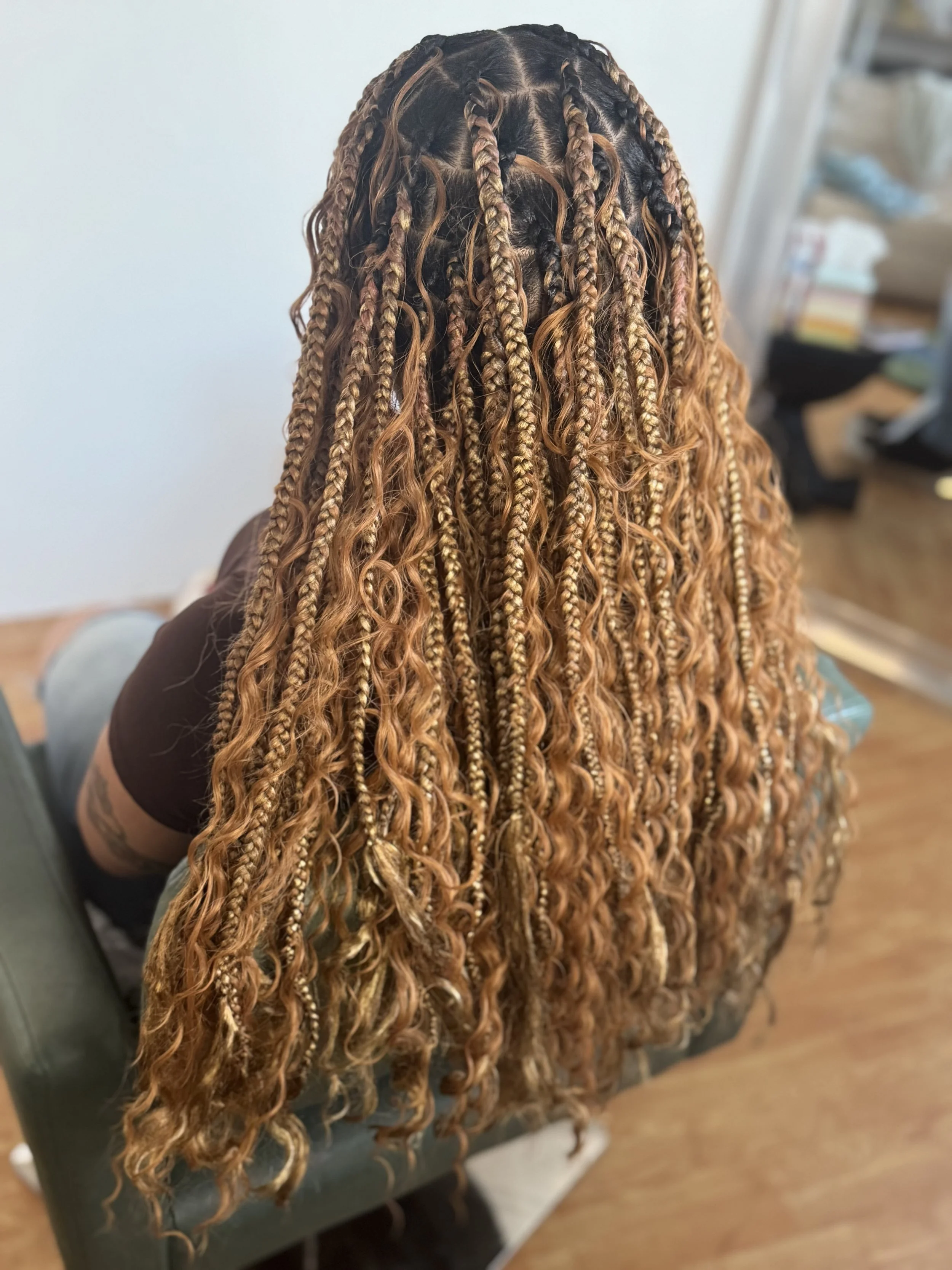 Back view of a woman with long, curly, two-tone blonde and dark brown knotless feed in braids that add extensions to waist length