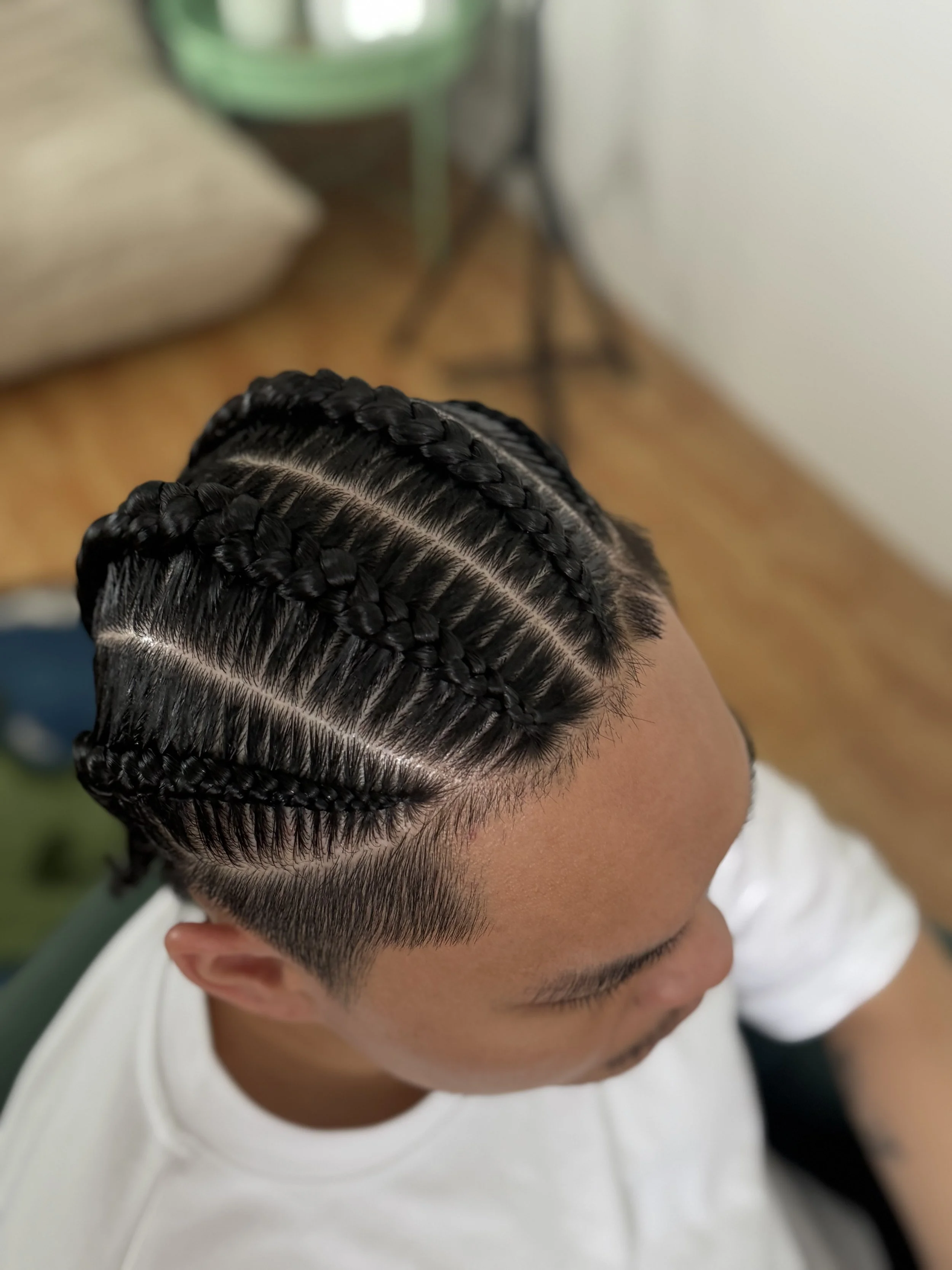 Top view of a man with neatly braided 4 cornrows hairstyle, showing the scalp and sleek, shiny hair.