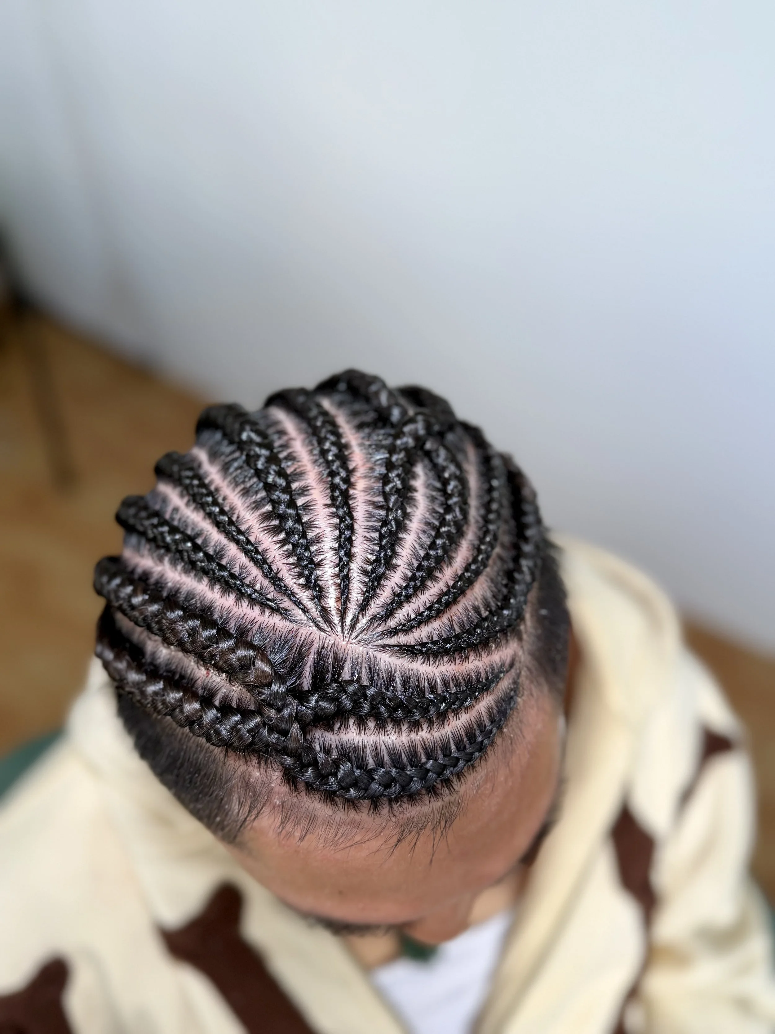Close-up of a person's scalp with tightly braided cornrows with a helix cross design, revealing sections of natural hair and scalp.