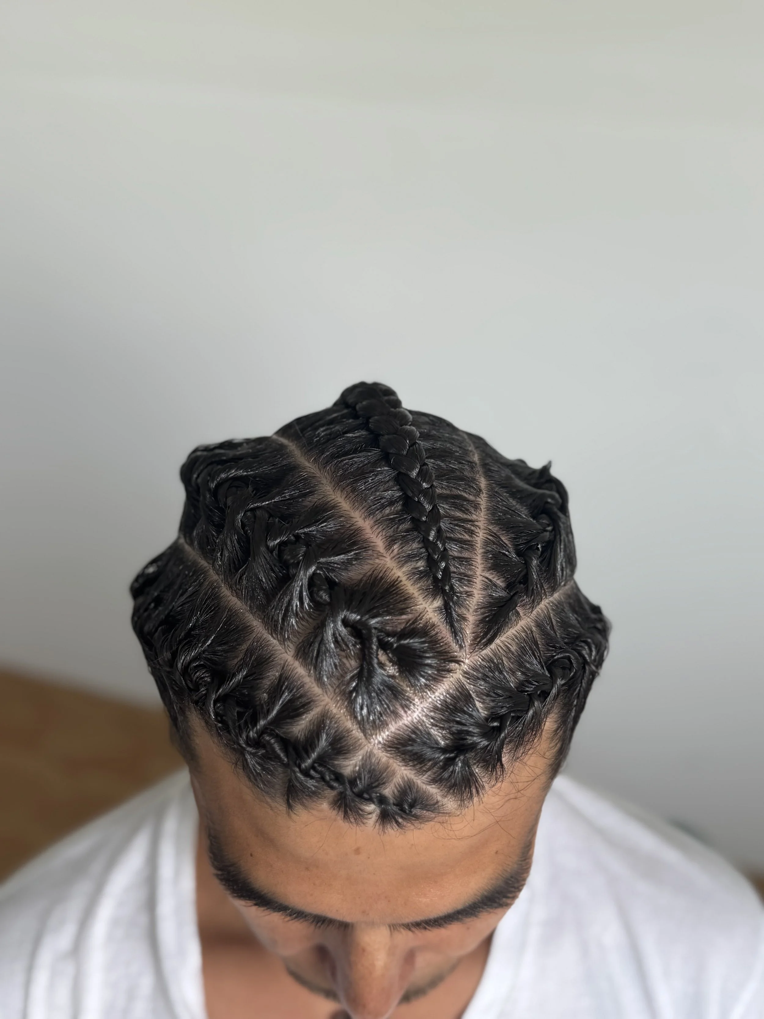 Top view of a man with intricately braided hairstyle featuring a combination of multiple barrel twists and a central braid.