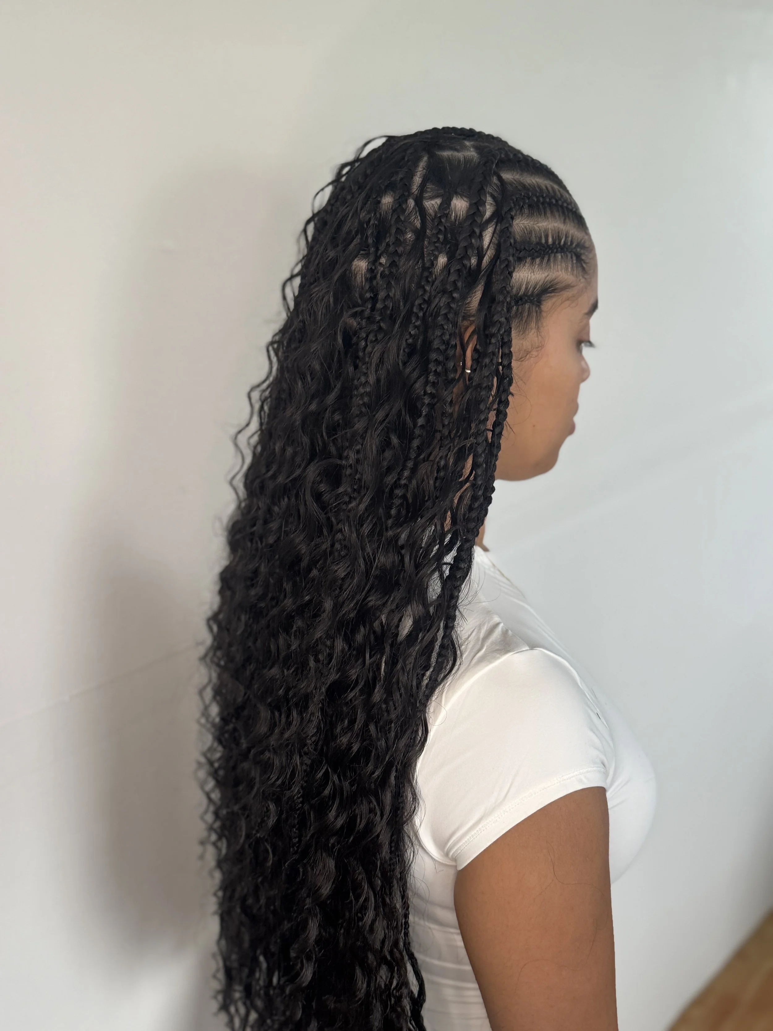 Side view of a woman with long, curly, and braided knotless feed in boho hair with fulani front braids for a protective style on her natural hair