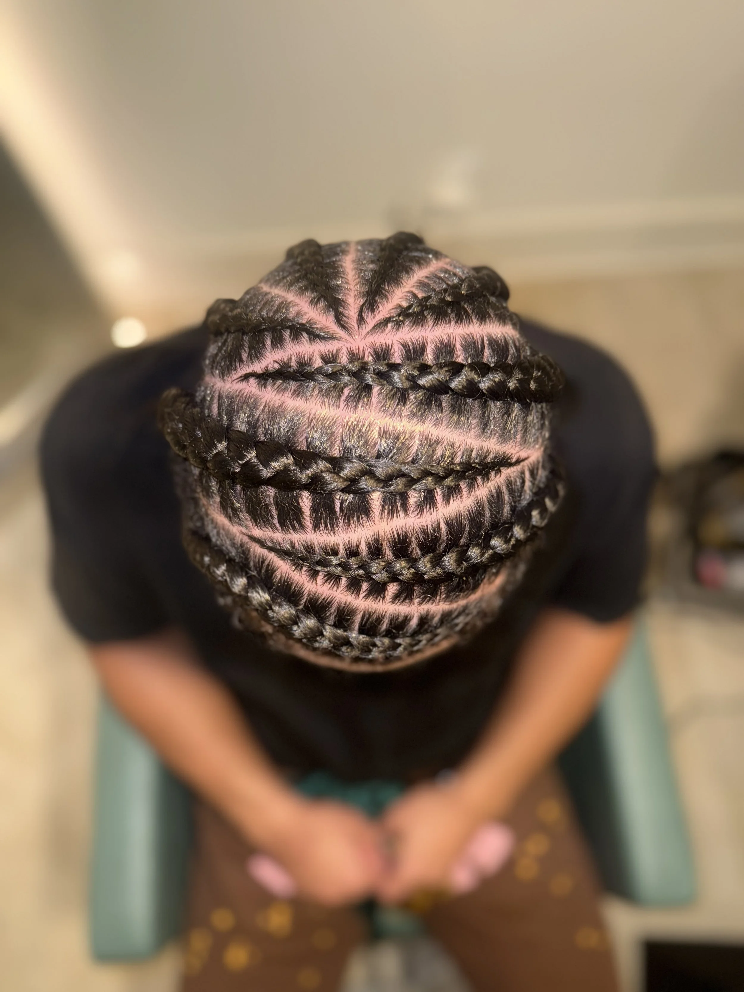 Top view of a person's head with braided hairstyle, showing intricate cornrows going down the side of the face