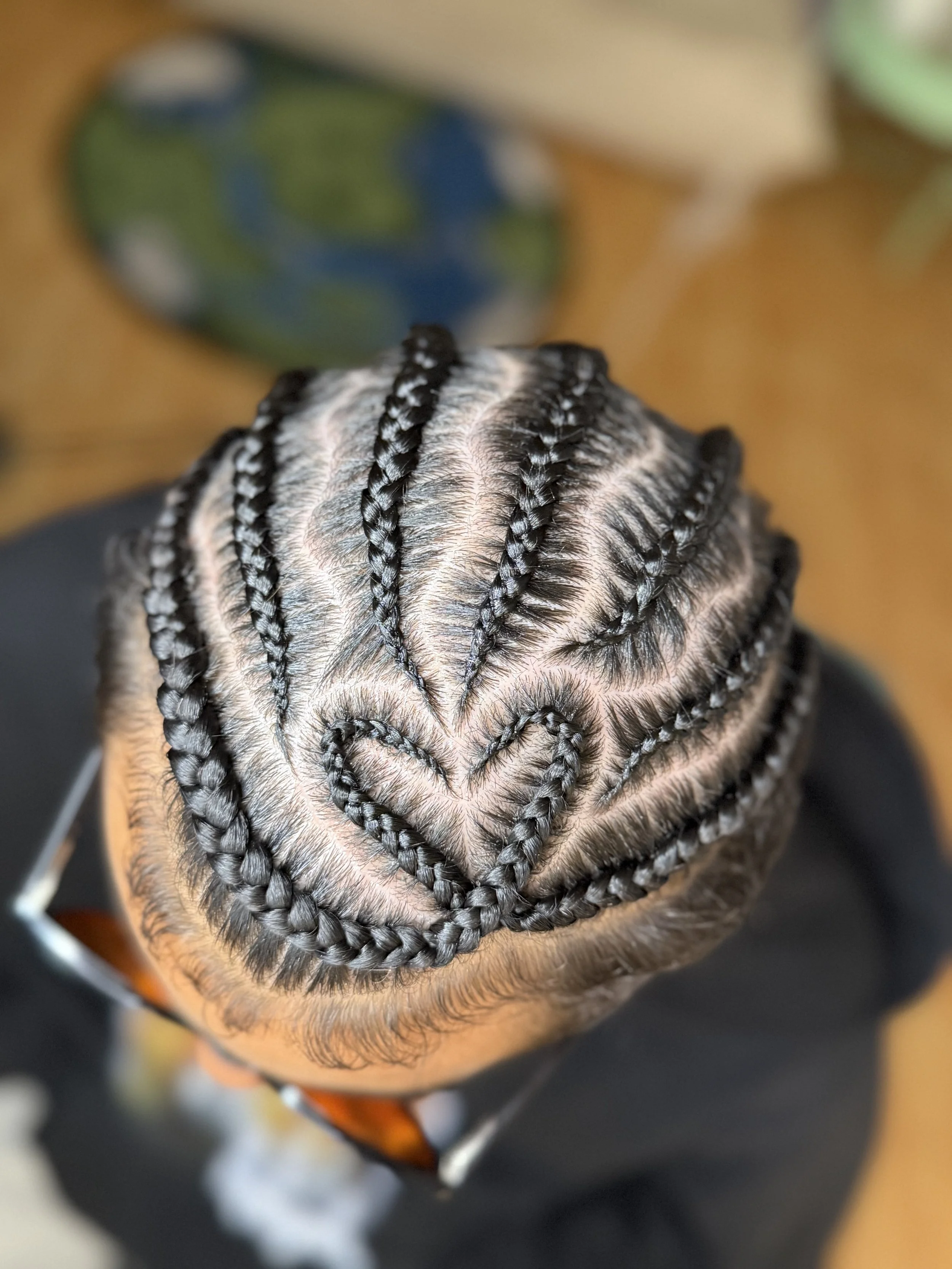 Top view of a person's head showing intricately styled tight cornrows design with squiggles and a heart design.