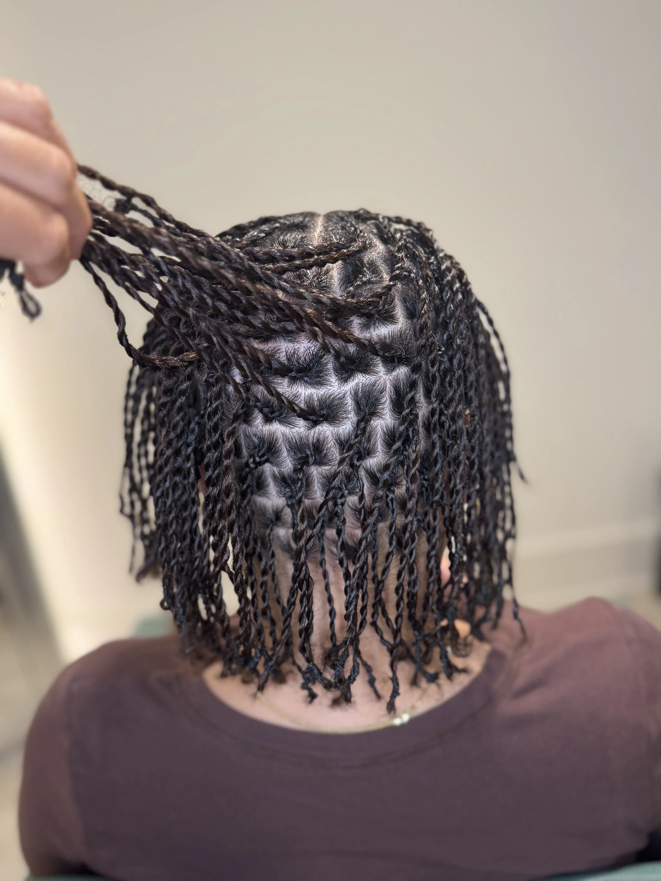 Person with short hair getting their hair styled with small, twisted braids.