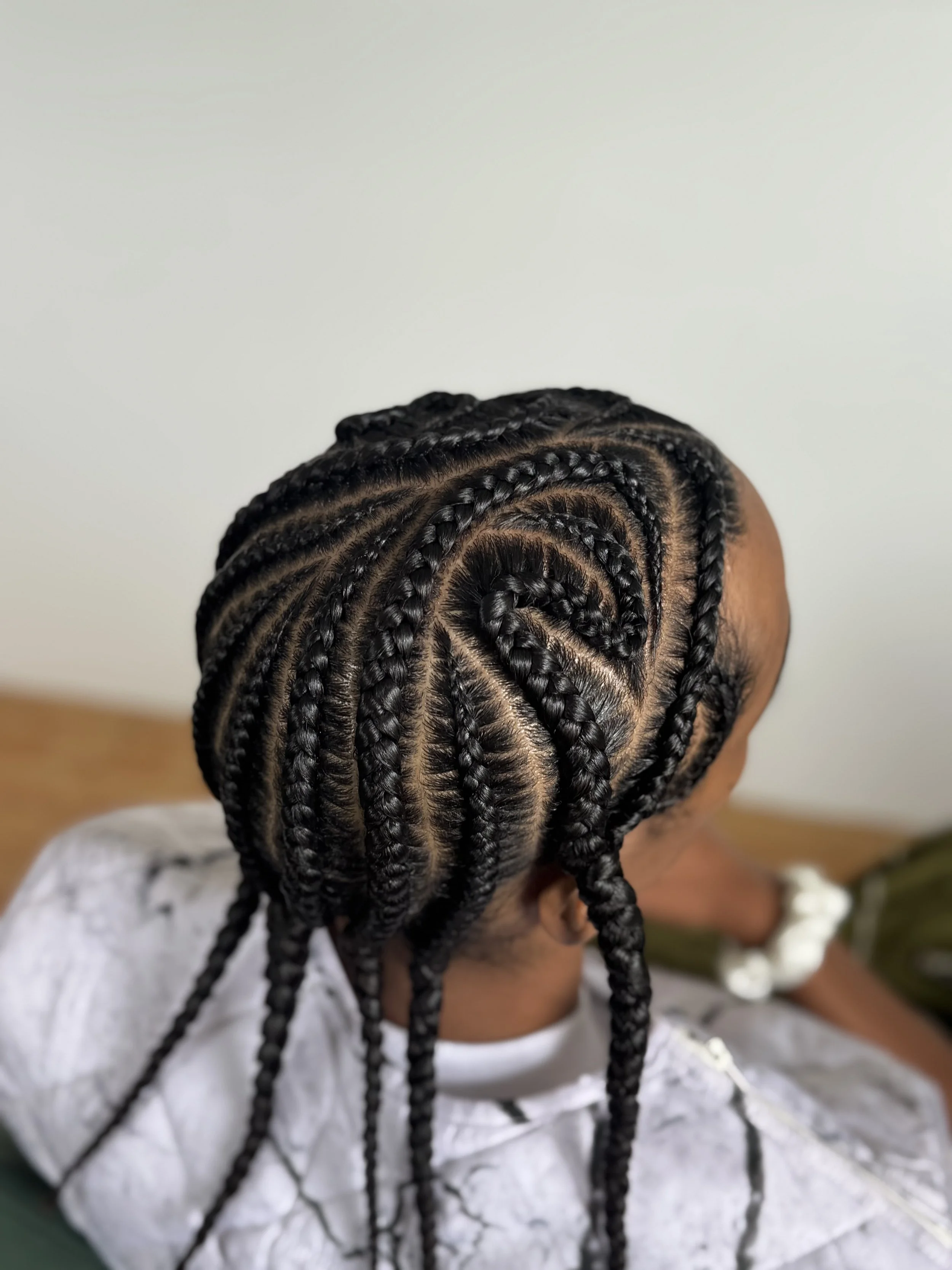 Close-up of a person's head with intricate braided hairstyle, styled in concentric circular patterns.