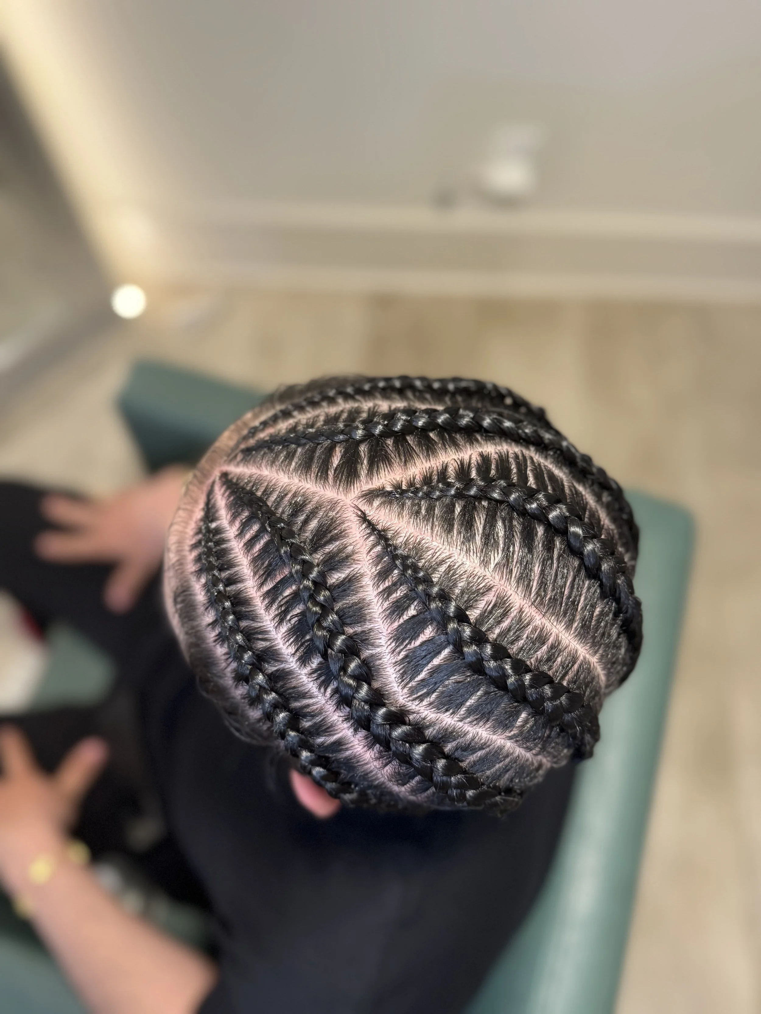 Top view of a person with intricate braided hairstyle, featuring multiple sections with stitch braids and linework