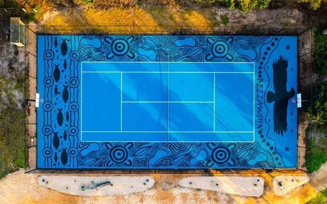 An aerial view of a decorated outdoor tennis court surrounded by a colorful mural with abstract patterns and a palm tree silhouette.